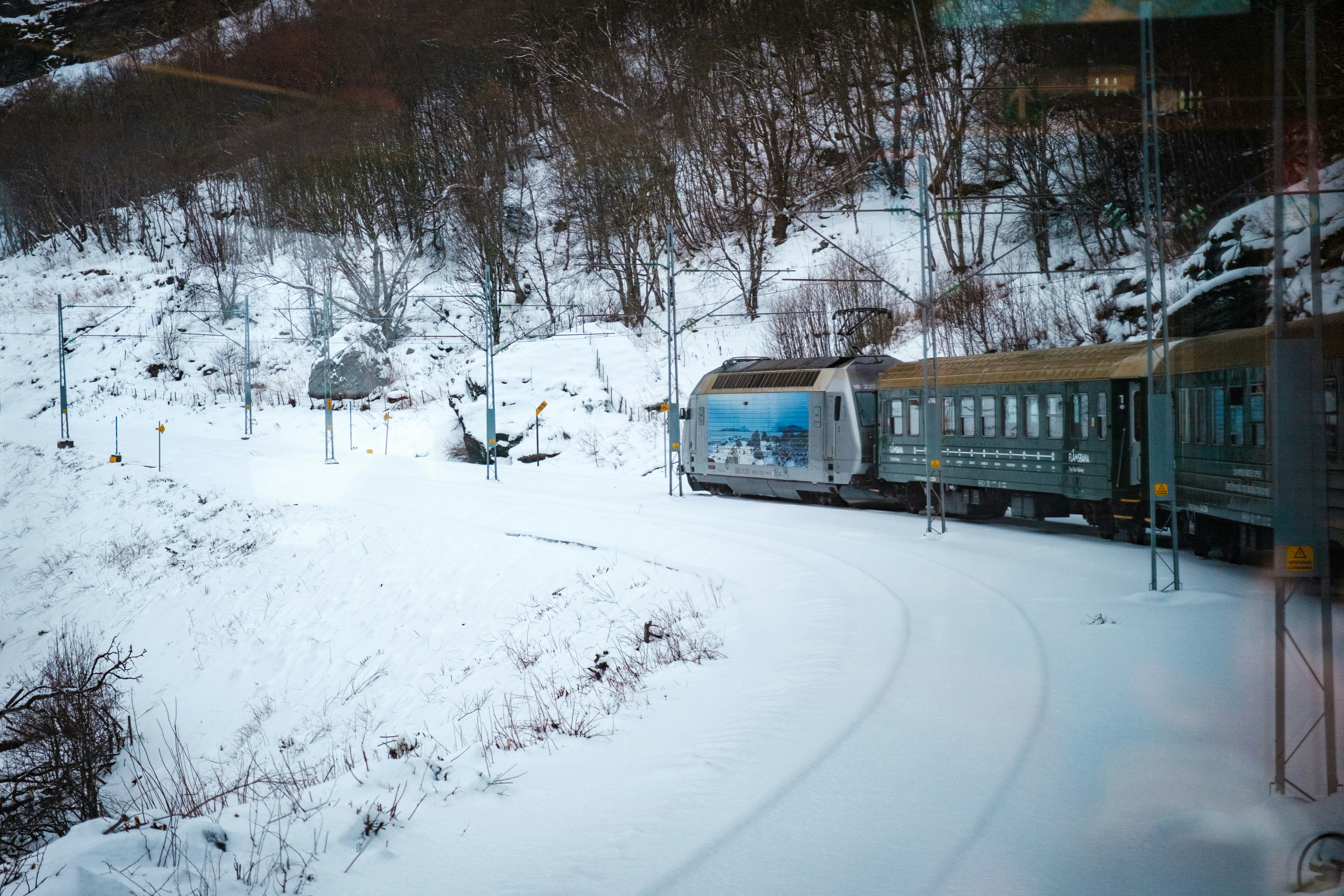a train traveling down tracks next to a snow covered hillside