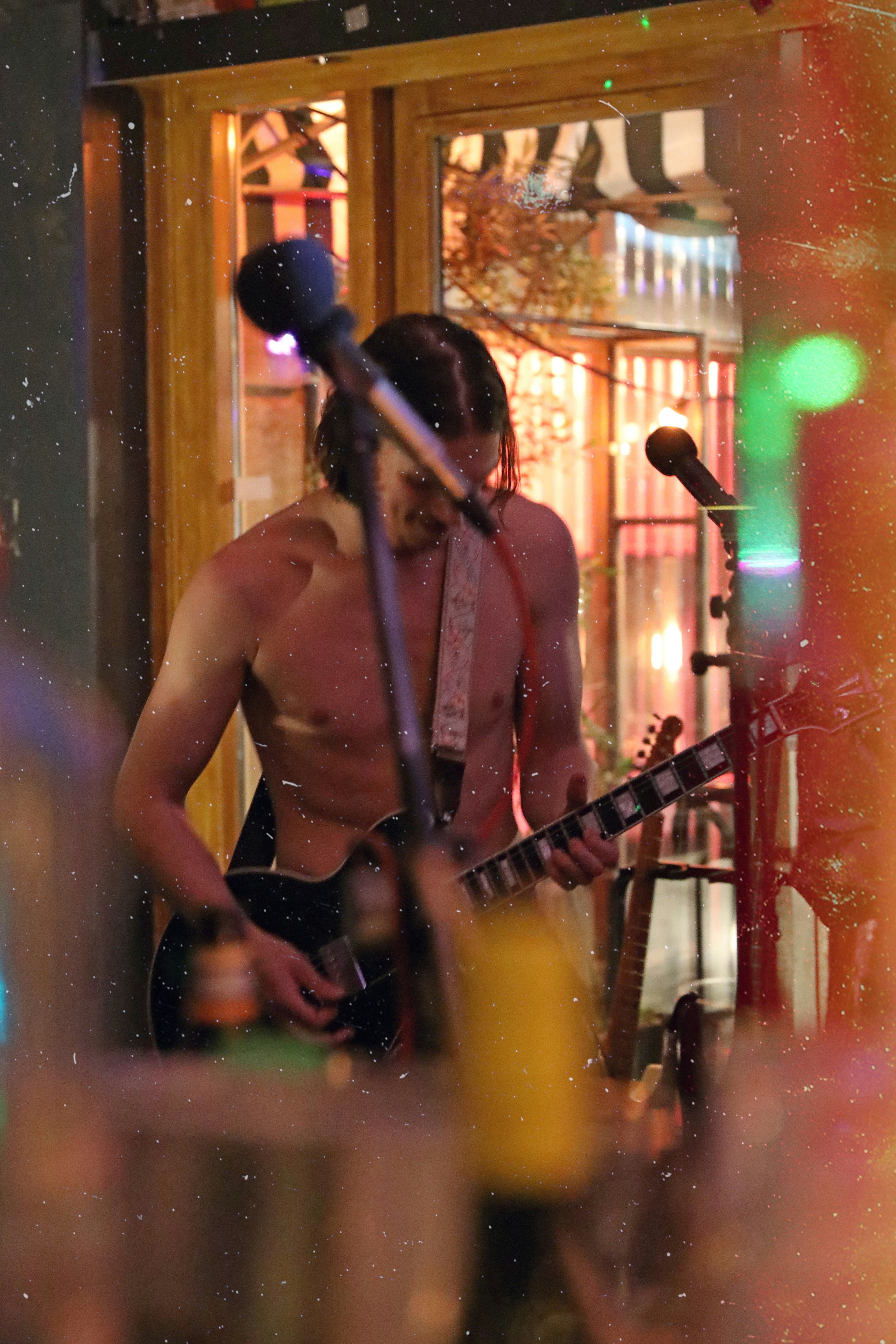 a shirtless man playing a guitar in front of a microphone