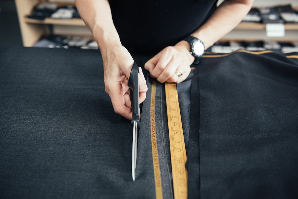 Tailor measuring and cutting dark cloth by hand on the atelier table