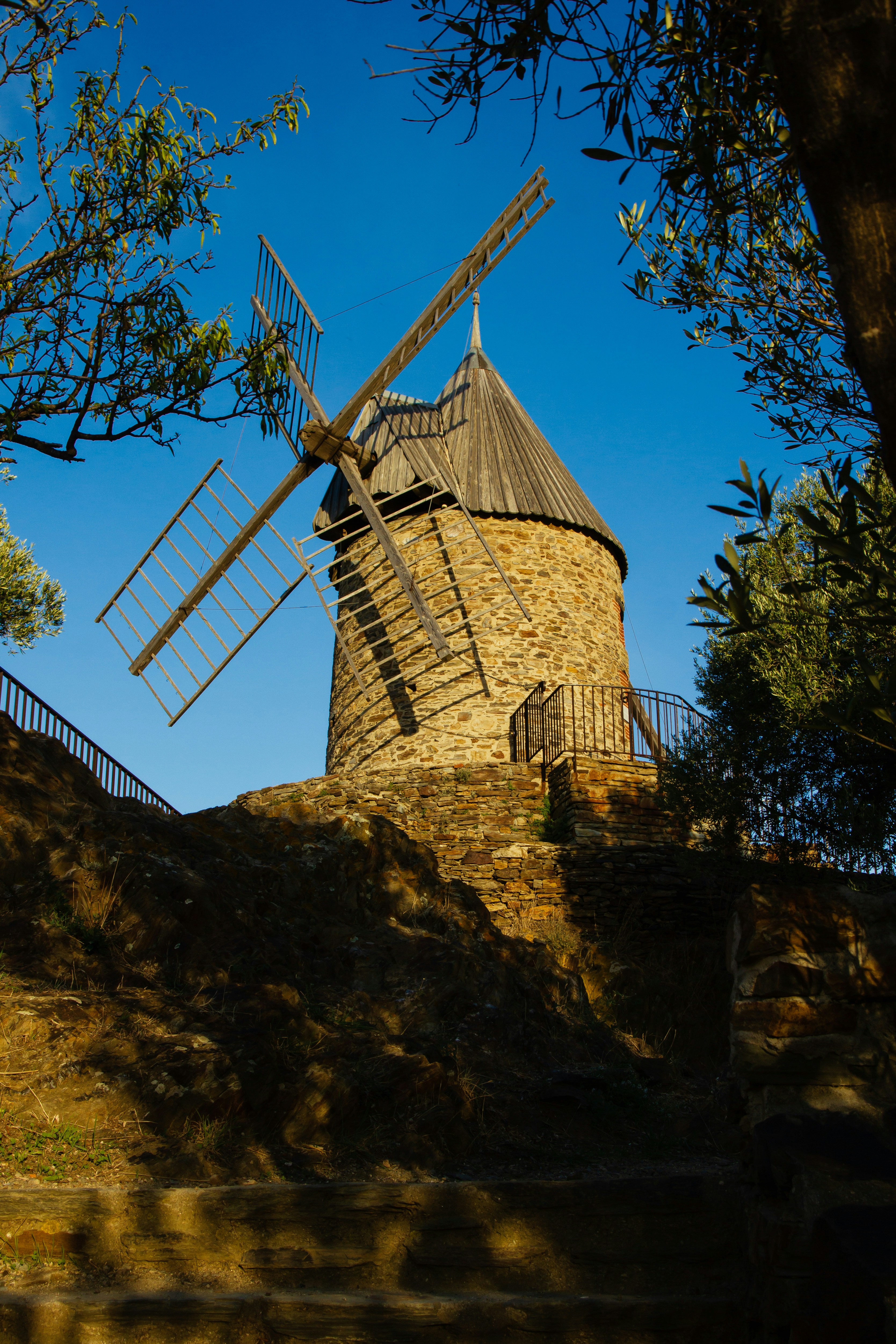 a windmill sitting on top of a hill next to a tree