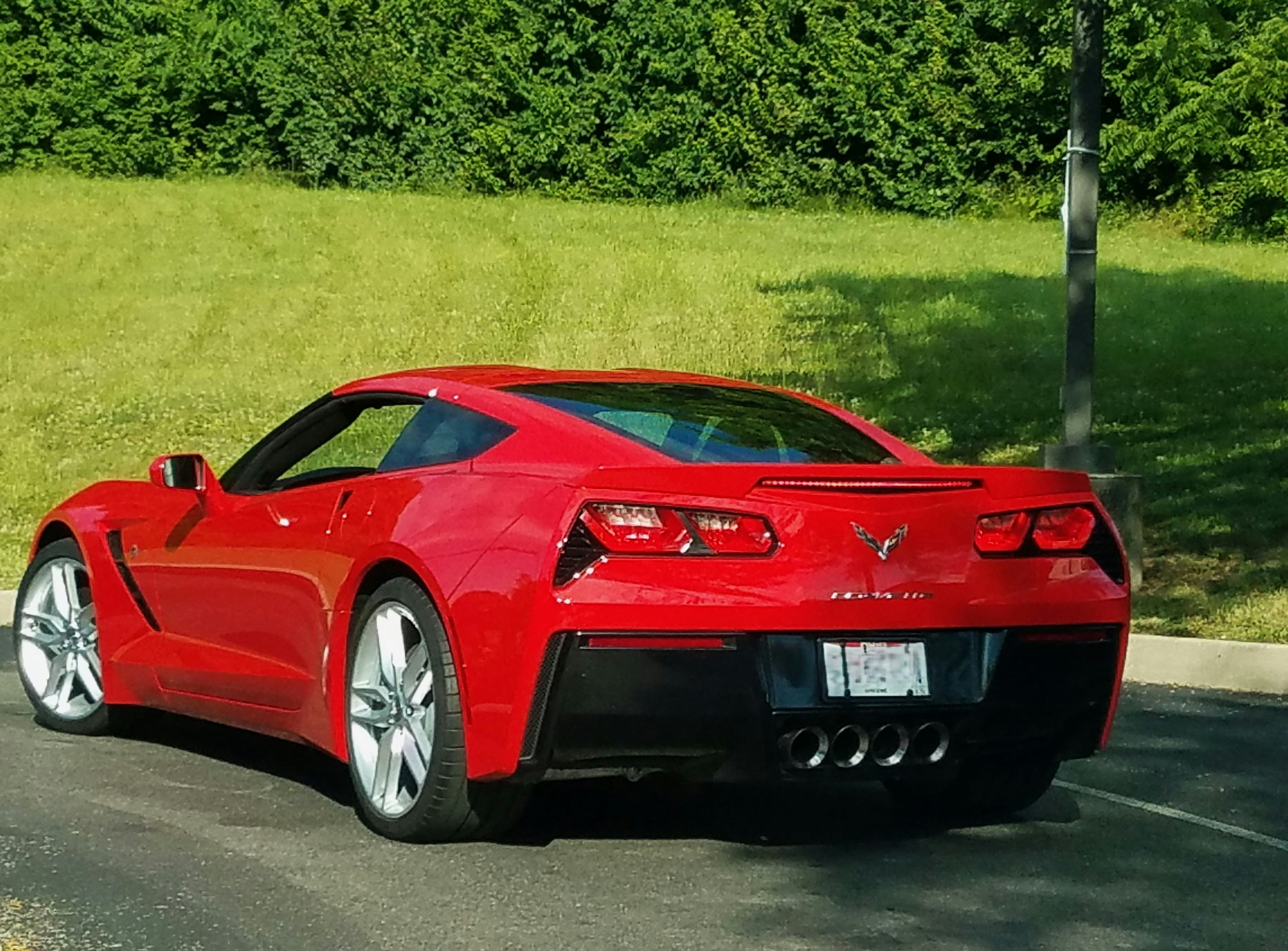 Red sports car with freshly polished paint reflecting sunlight on clean asphalt, dark background