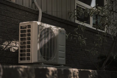 Residential outdoor air conditioning condenser beside a brick house wall.