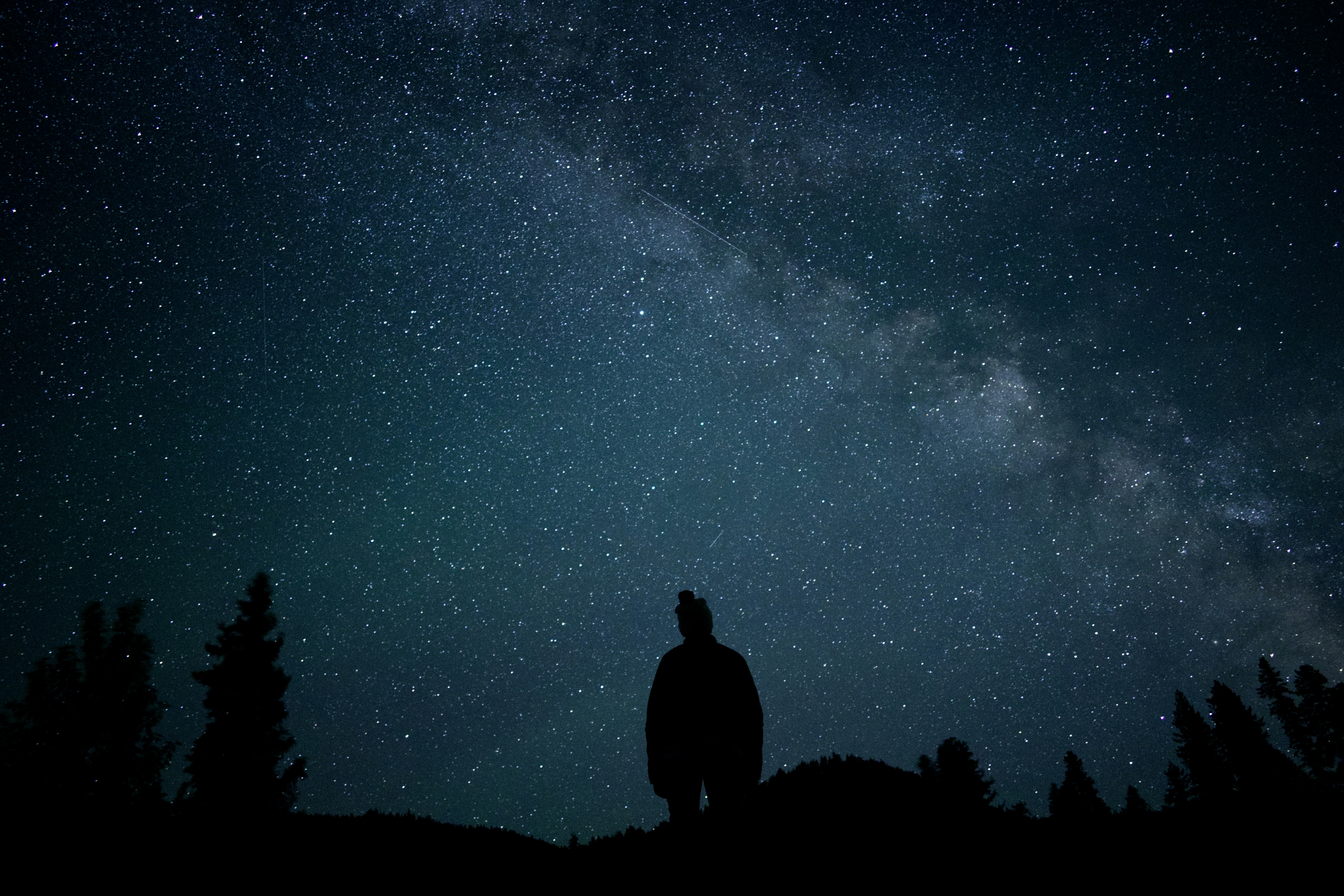 un uomo in piedi sulla cima di una collina sotto un cielo notturno pieno di stelle