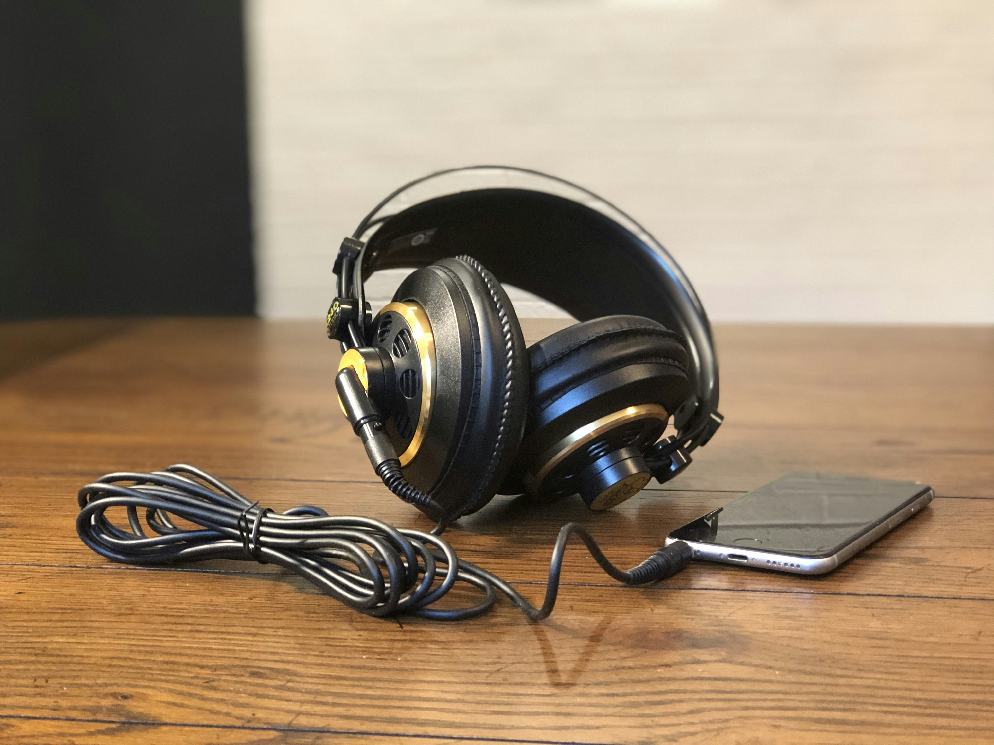 Semi-open back studio headphones with a cable attached to an iPhone, all resting on a wooden table