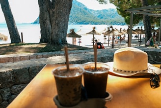 a table with two drinks and a hat on it looking toward the bay of pollensa mallorca