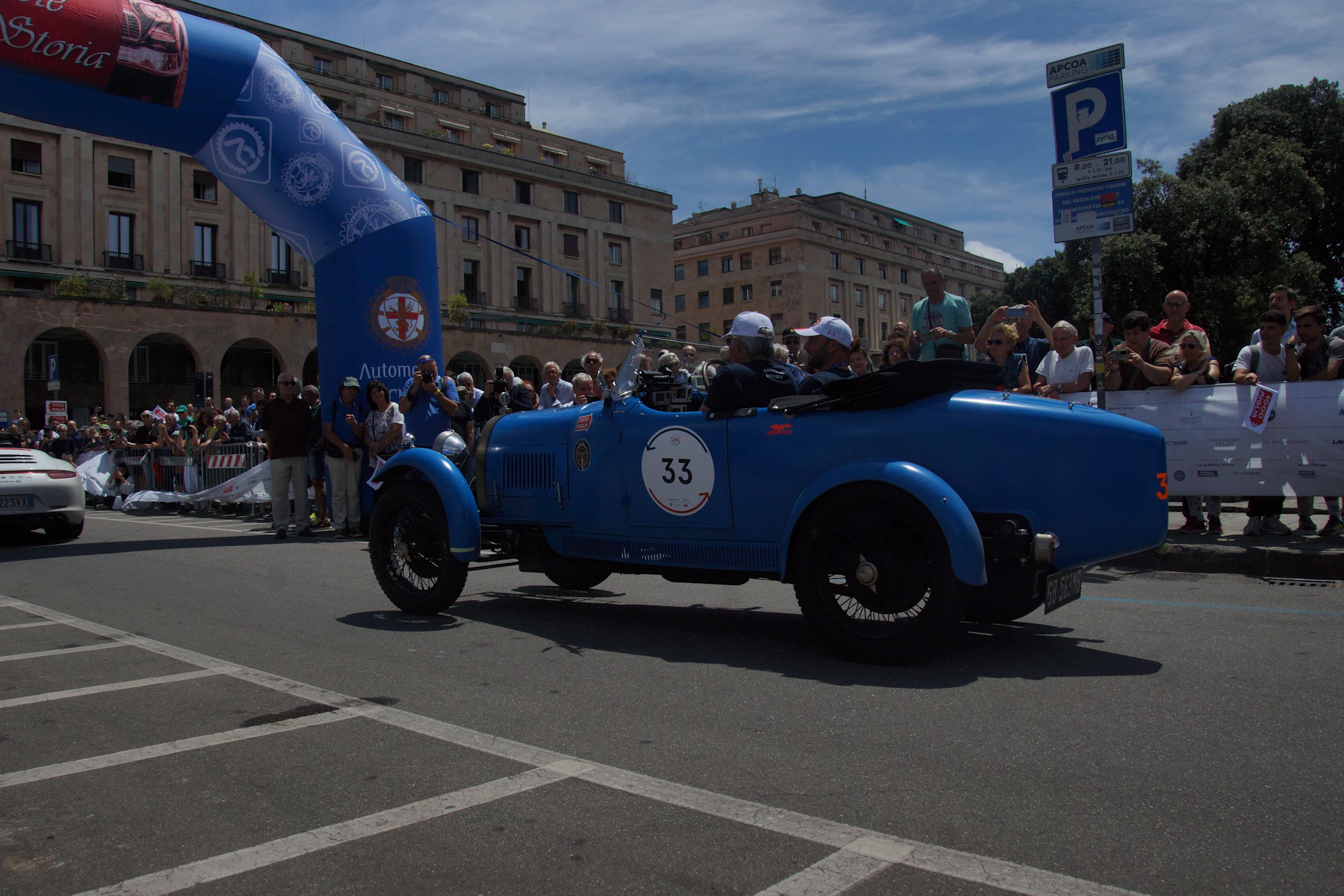 a blue car driving down a street next to a crowd of people