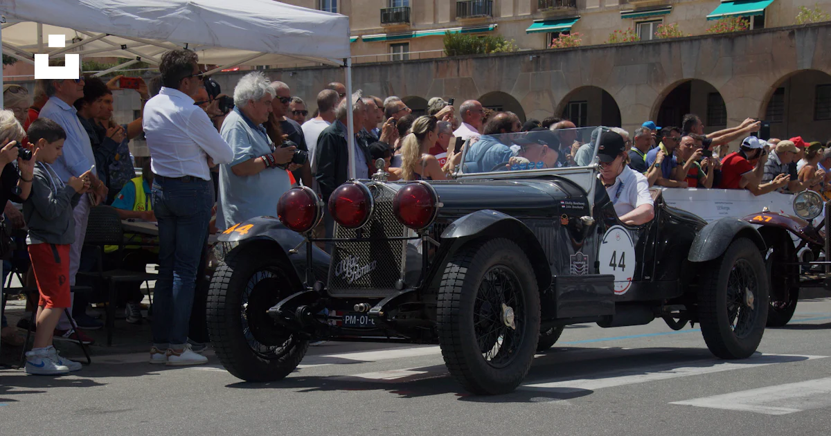 A vintage car driving down a street past a crowd of people photo – Free ...