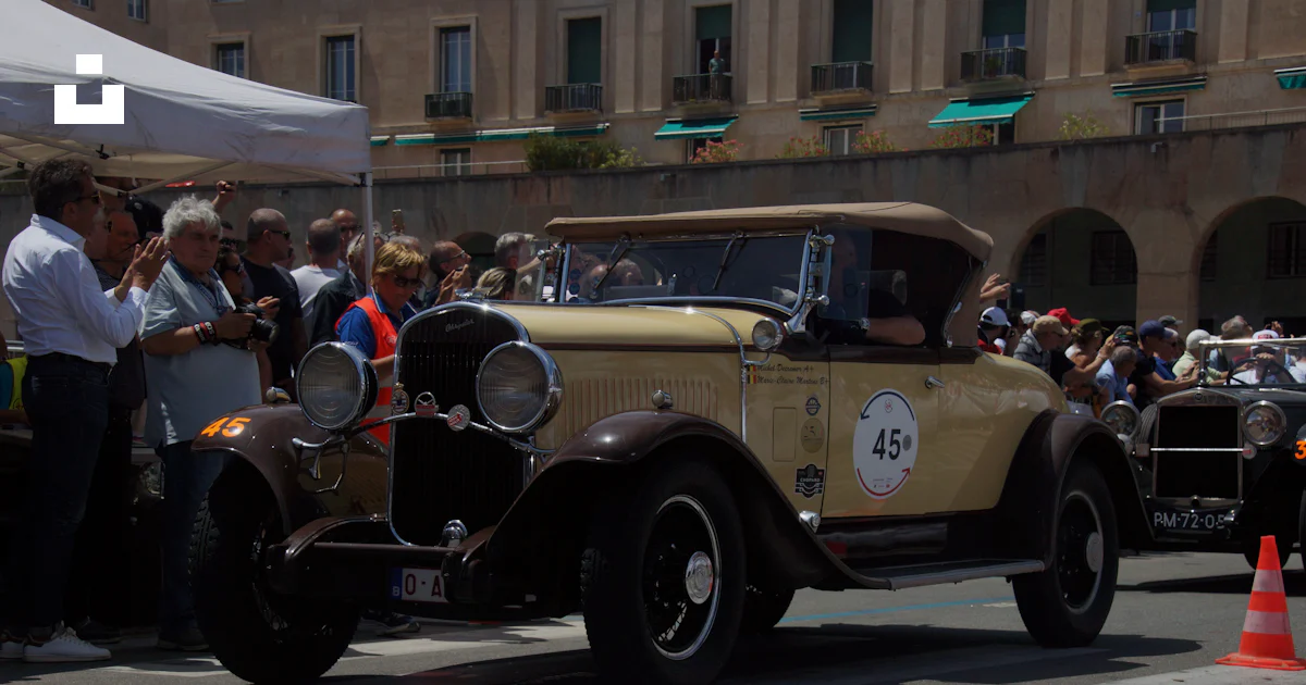 A vintage car driving down a street past a crowd of people photo – Free ...