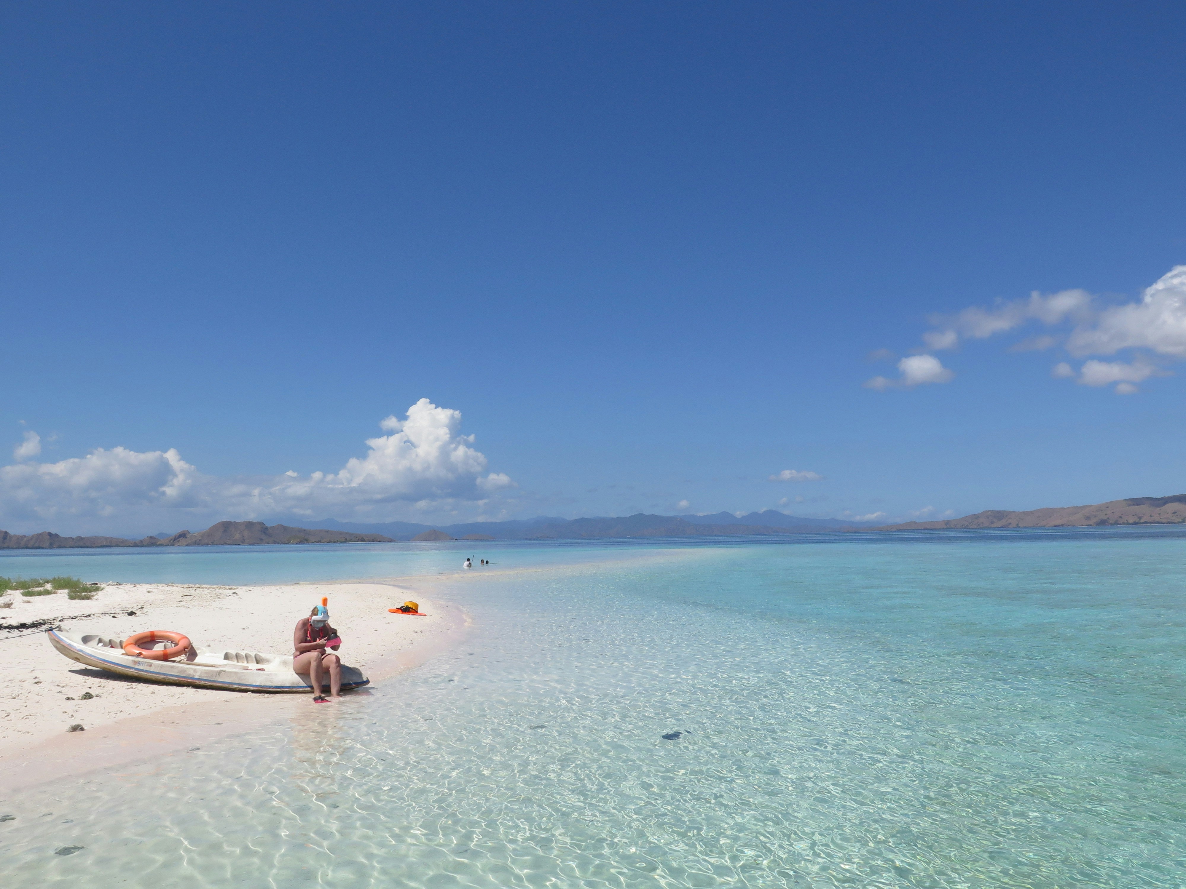 a person sitting on a boat on a beach, A woman on the sand island going snorkelling