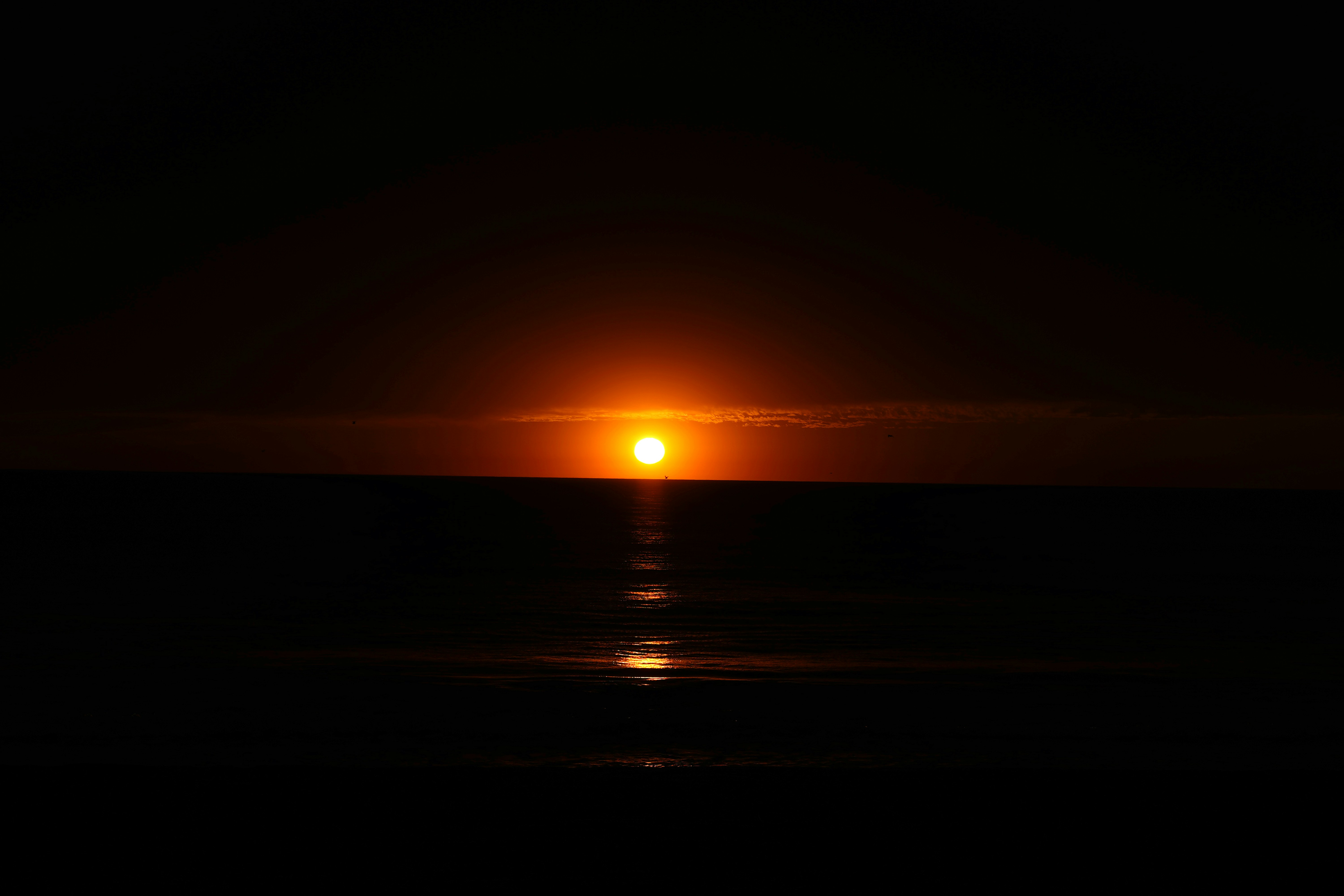 the sun is setting over the ocean in the dark