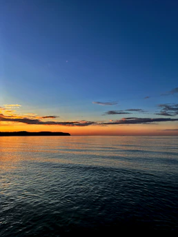 the sun is setting over the ocean with a boat in the distance