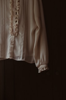 a white blouse with ruffles hanging from a hook