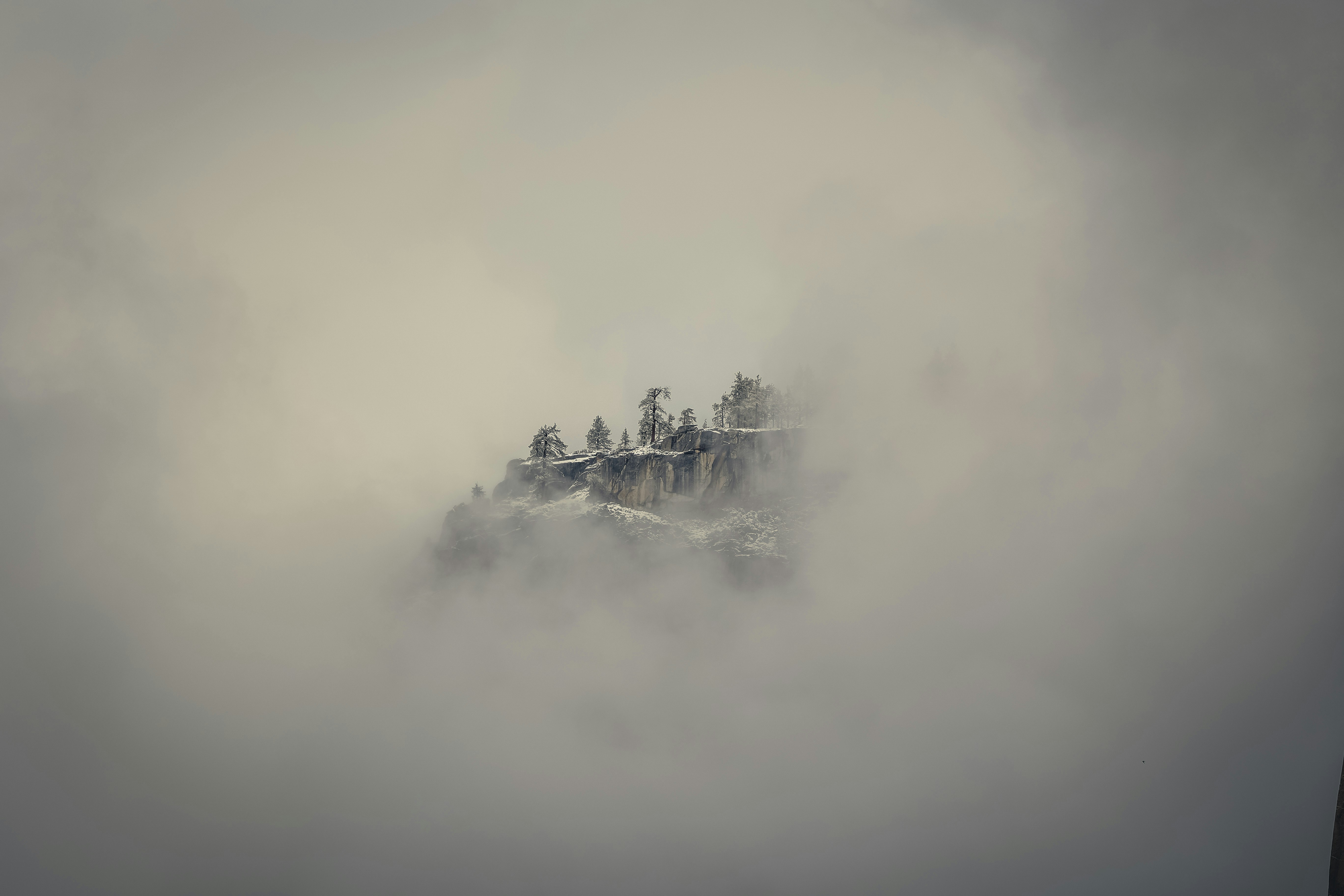 a mountain covered in fog with trees on top of it