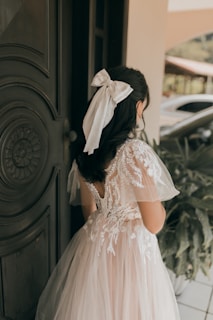 a little girl in a white dress standing in front of a door
