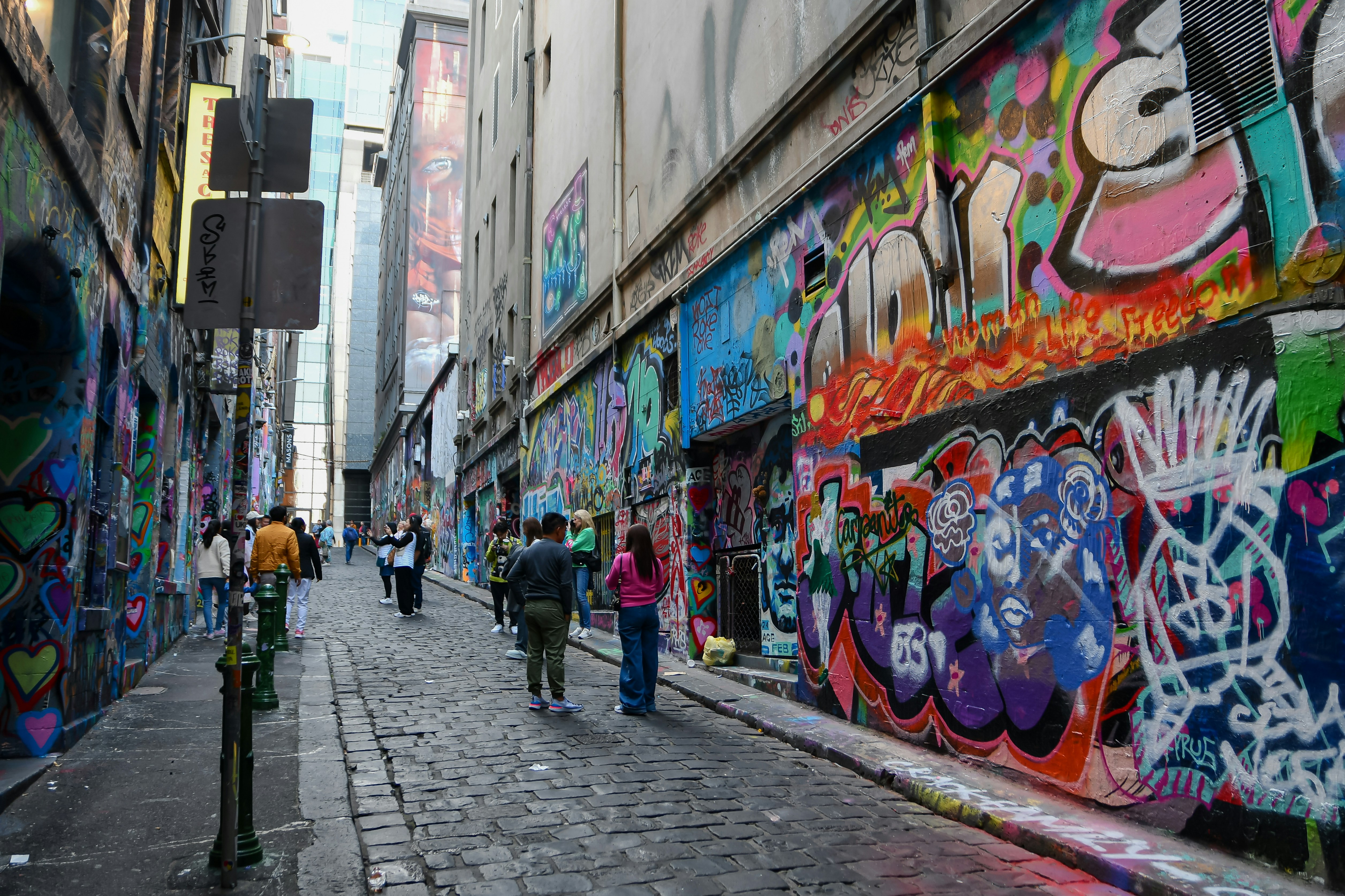 a group of people walking down a street next to a wall covered in graffiti