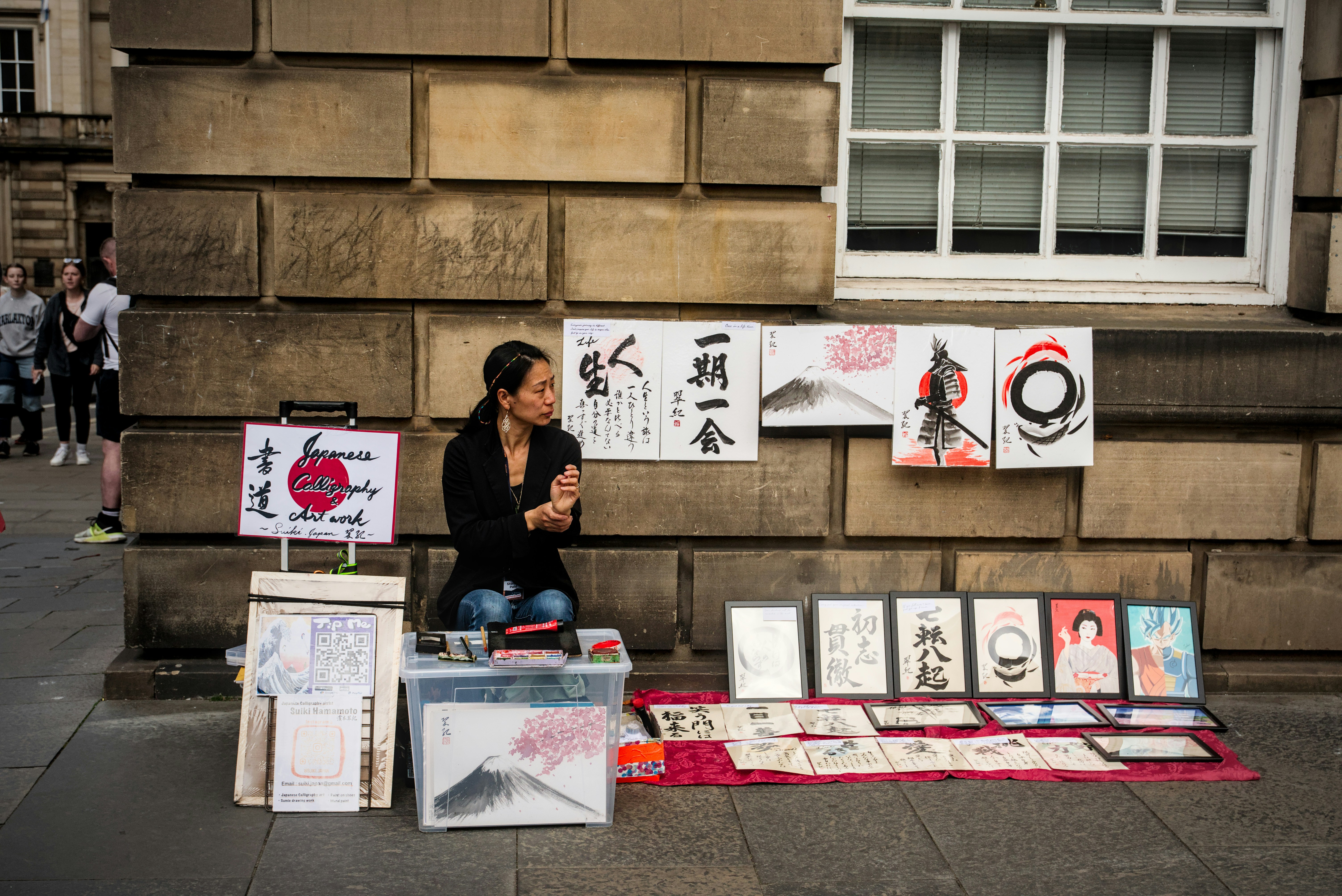 A woman sitting on a sidewalk next to a display of cards