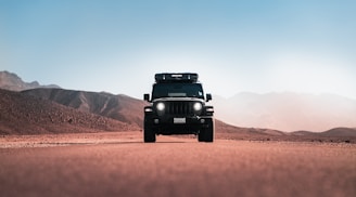 a jeep driving down a desert road with mountains in the background