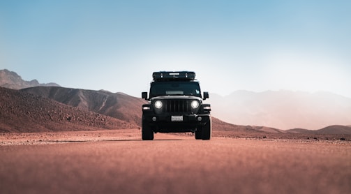 a jeep driving down a desert road with mountains in the background