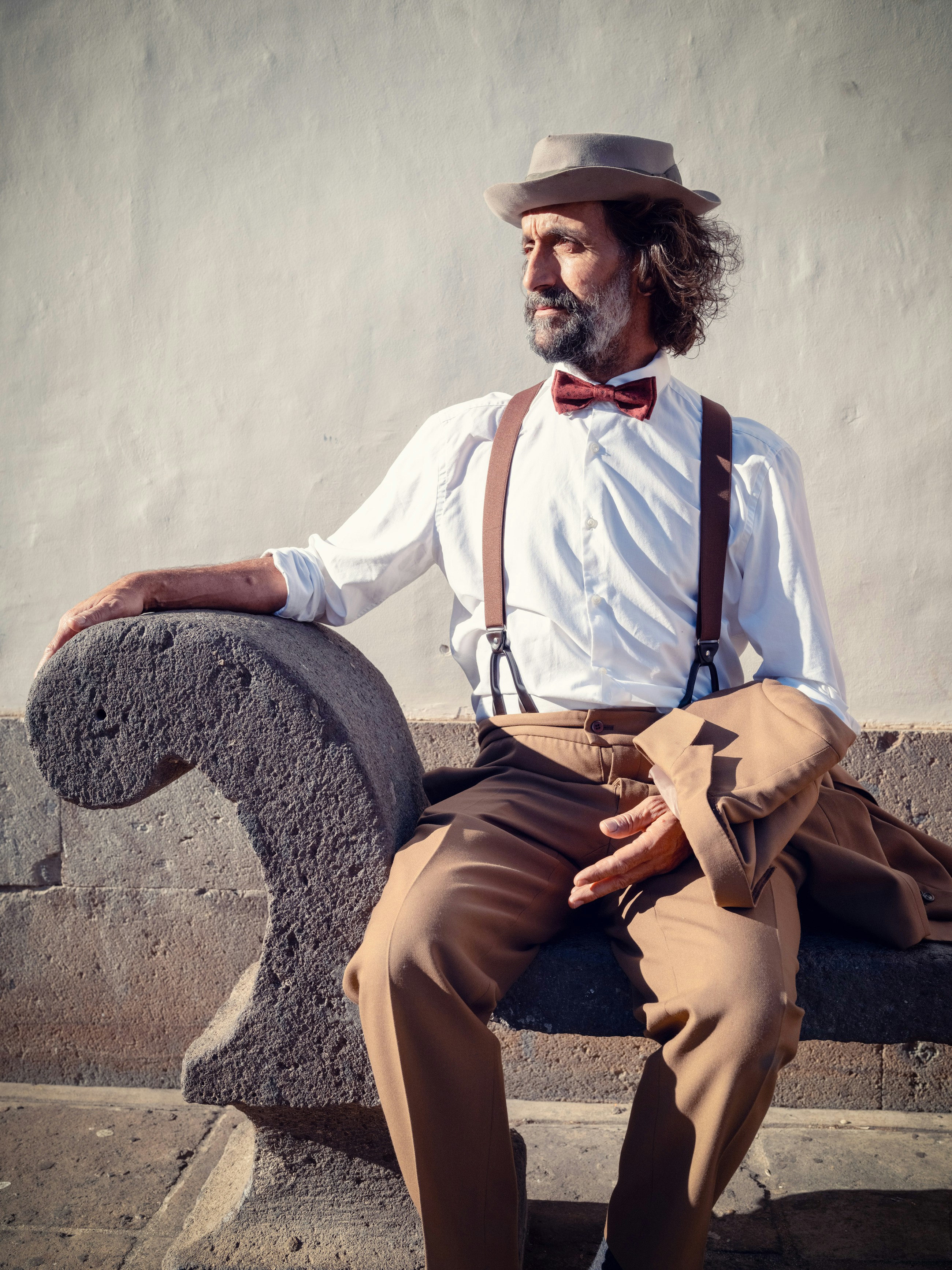 un uomo che indossa un cappello e bretelle seduto su una panchina
