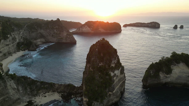 The sun is setting over the ocean with rocks in the water