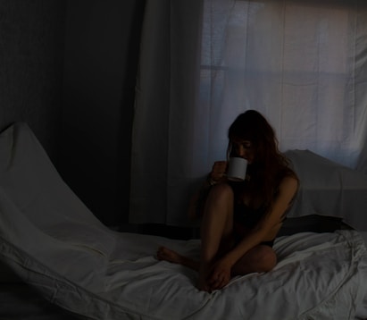 a woman sitting on a bed drinking a cup of coffee