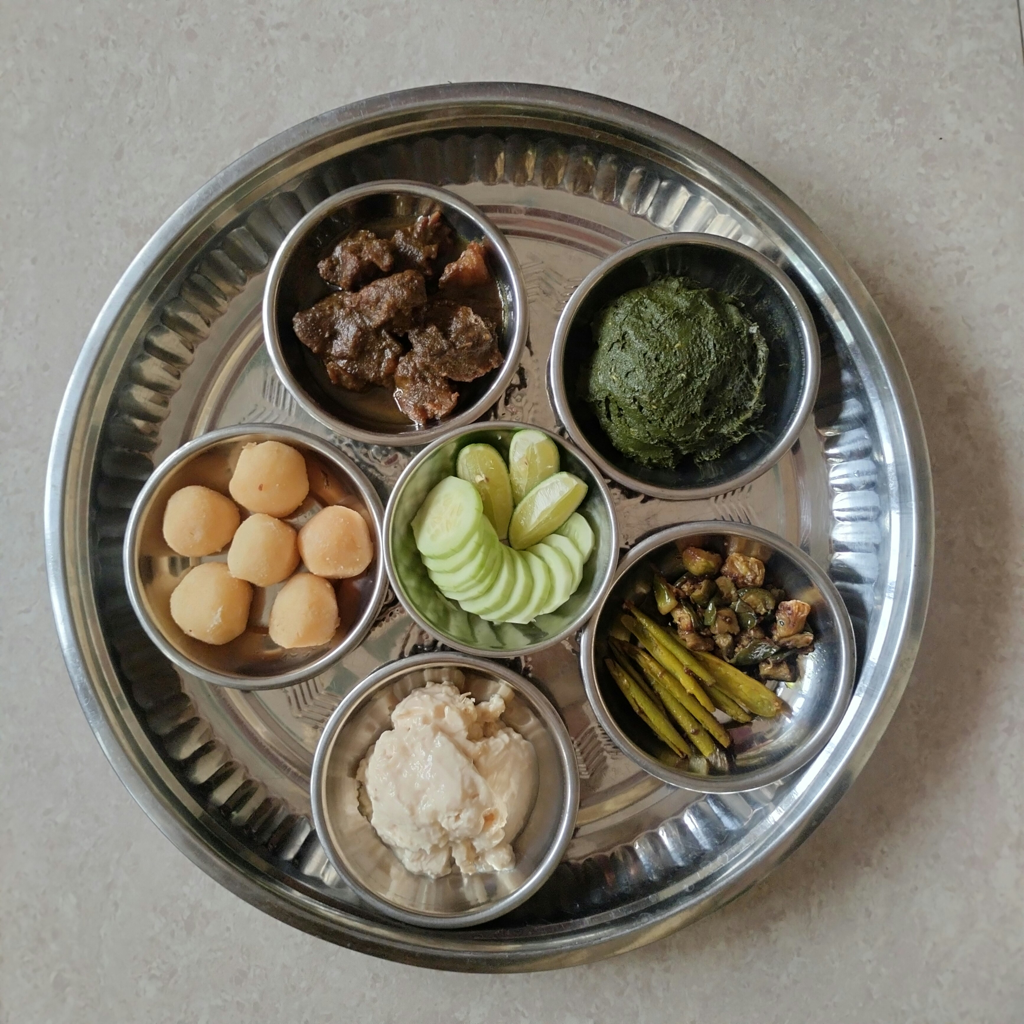 Traditional Indian thali with multiple colorful vegetarian dishes arranged in brass bowls on a large silver plate, overhead view