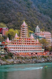 a boat traveling down a river ganga next to a Temple in Rishikesh