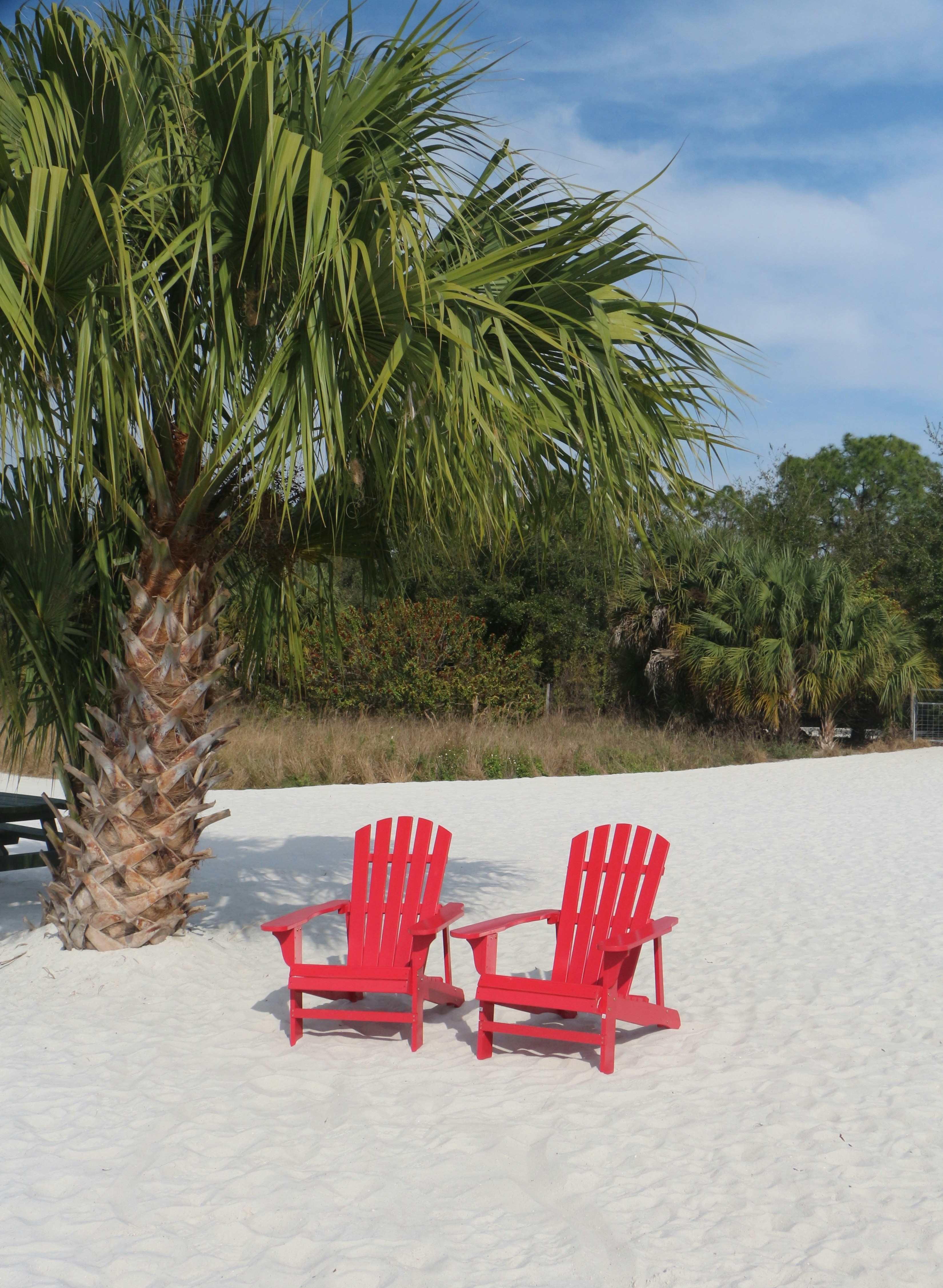 a couple of red chairs sitting on top of a sandy beach