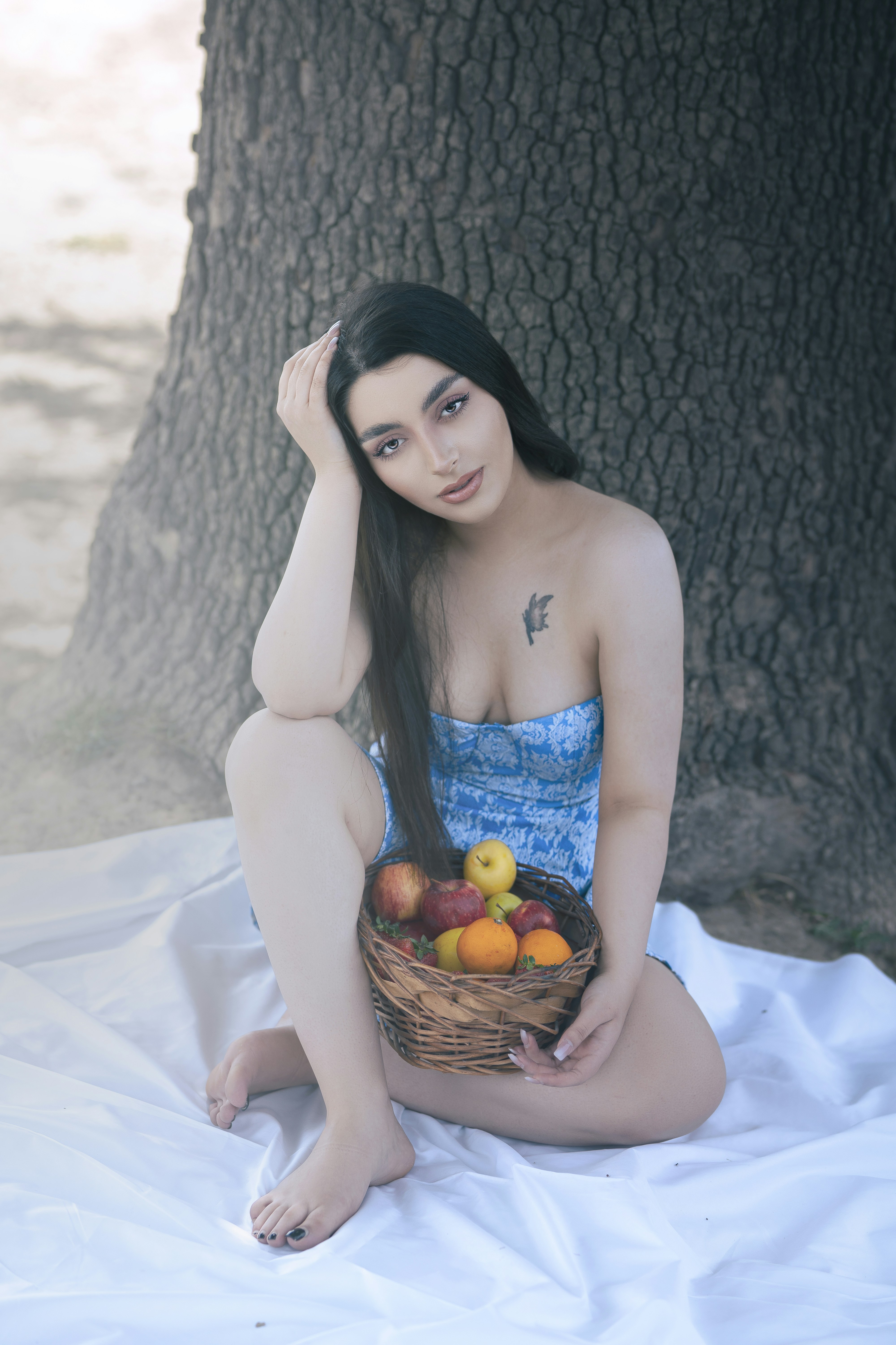 a woman sitting on a blanket holding a basket of fruit