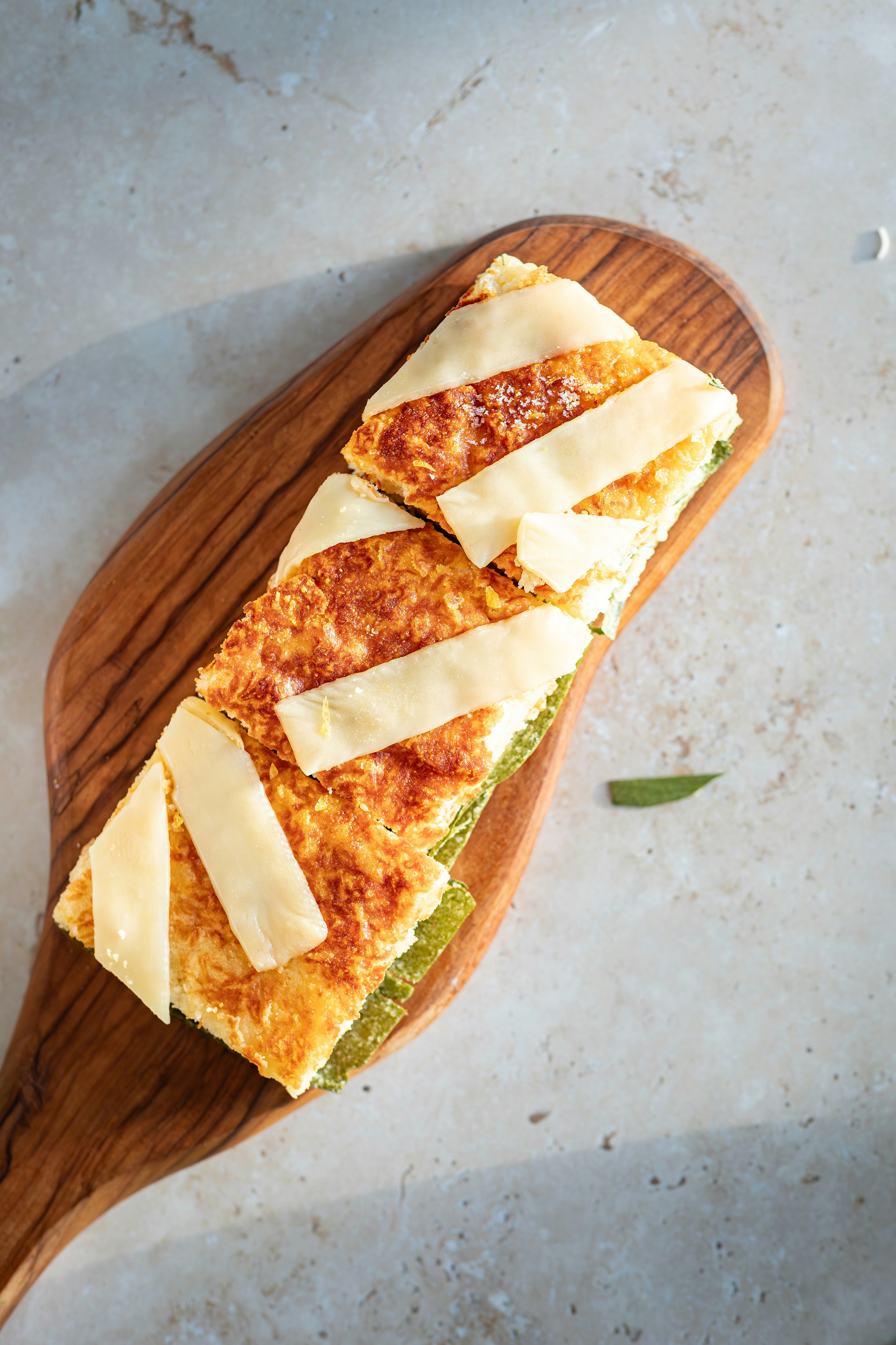 Golden-brown baked dish slices with cheese strips on a wooden board.