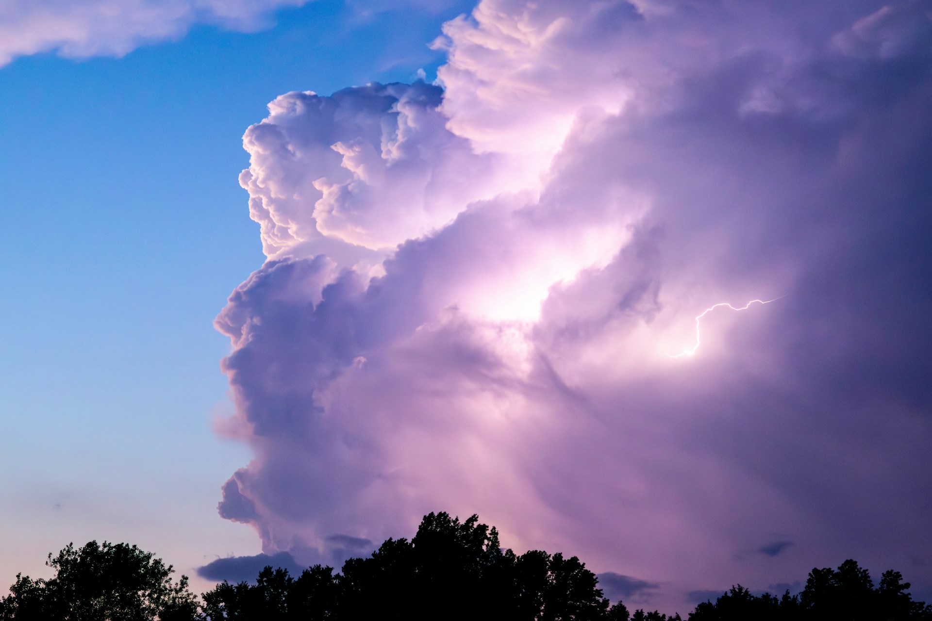a large cloud is in the sky above some trees