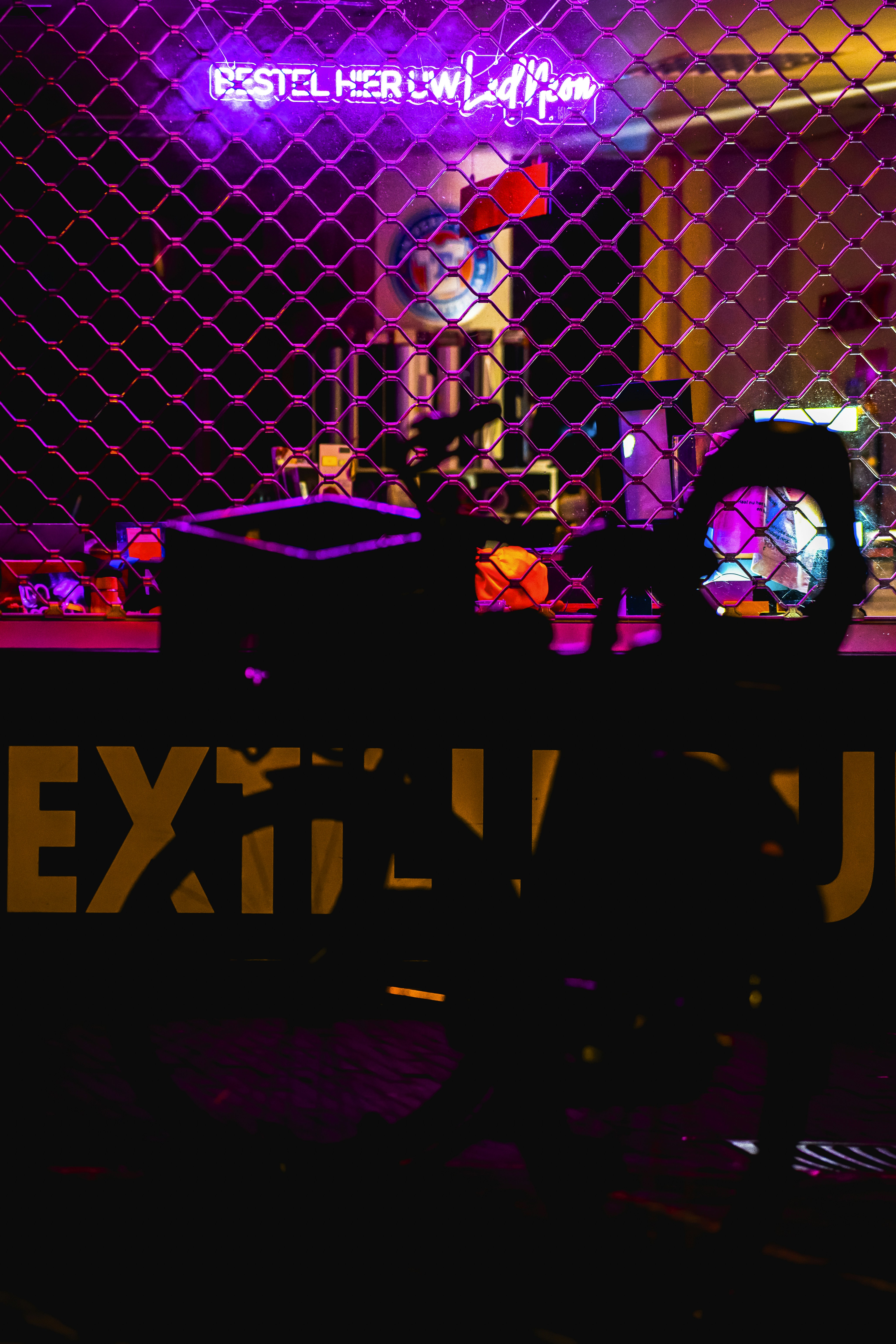 a neon sign behind a chain link fence