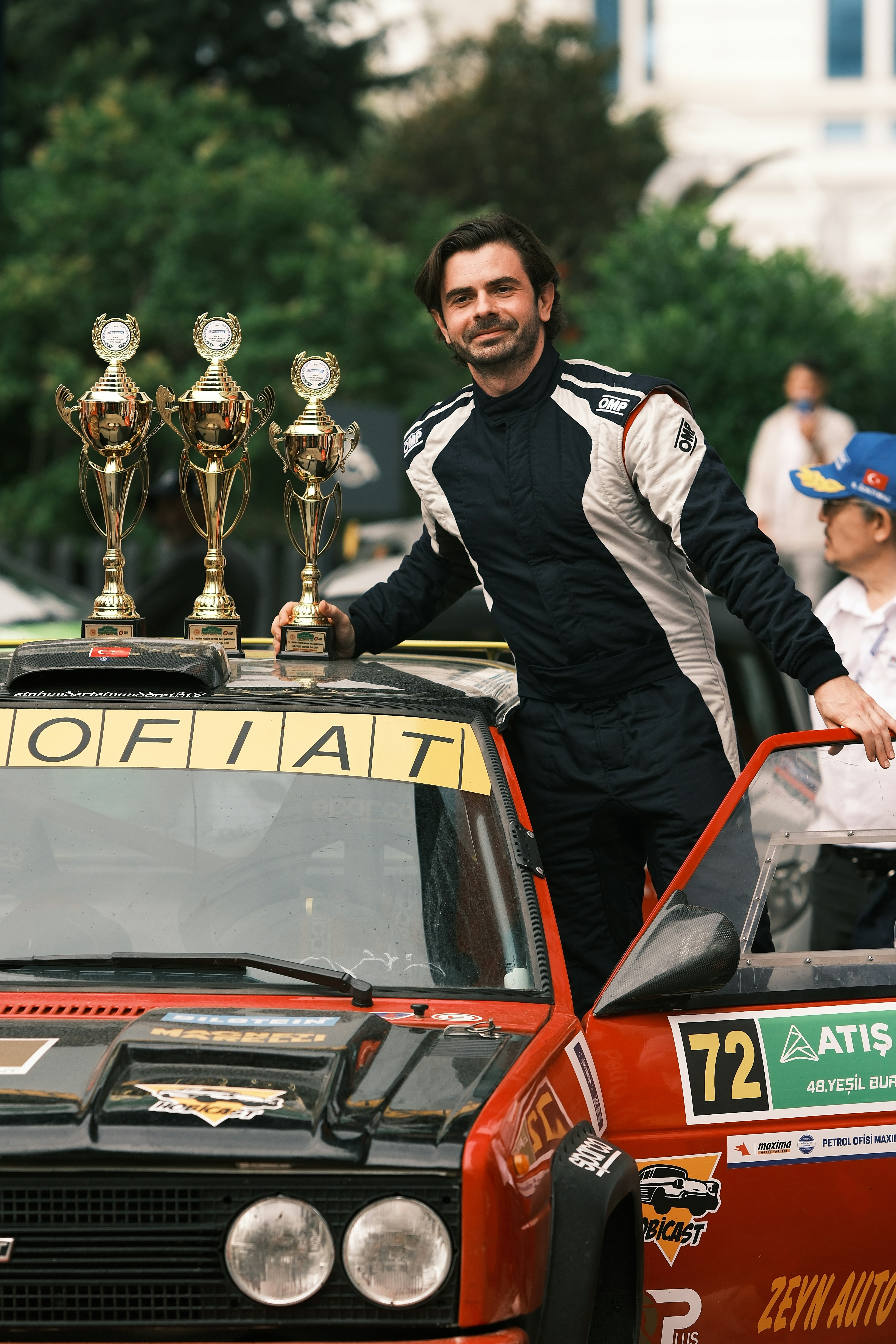 A man standing on top of a car with trophies on top of it