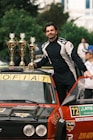 A man standing on top of a car with trophies on top of it