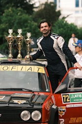 A man standing on top of a car with trophies on top of it