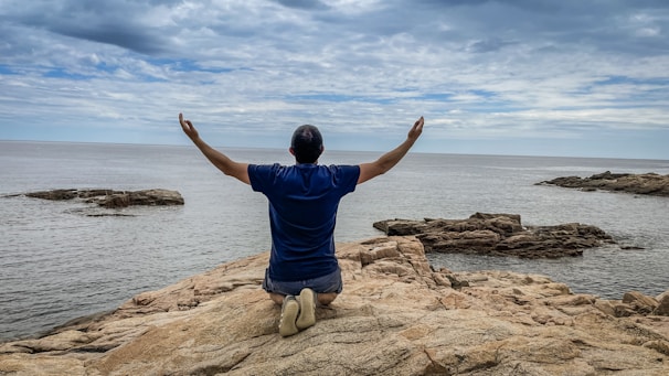 a man sitting on top of a rock near the ocean