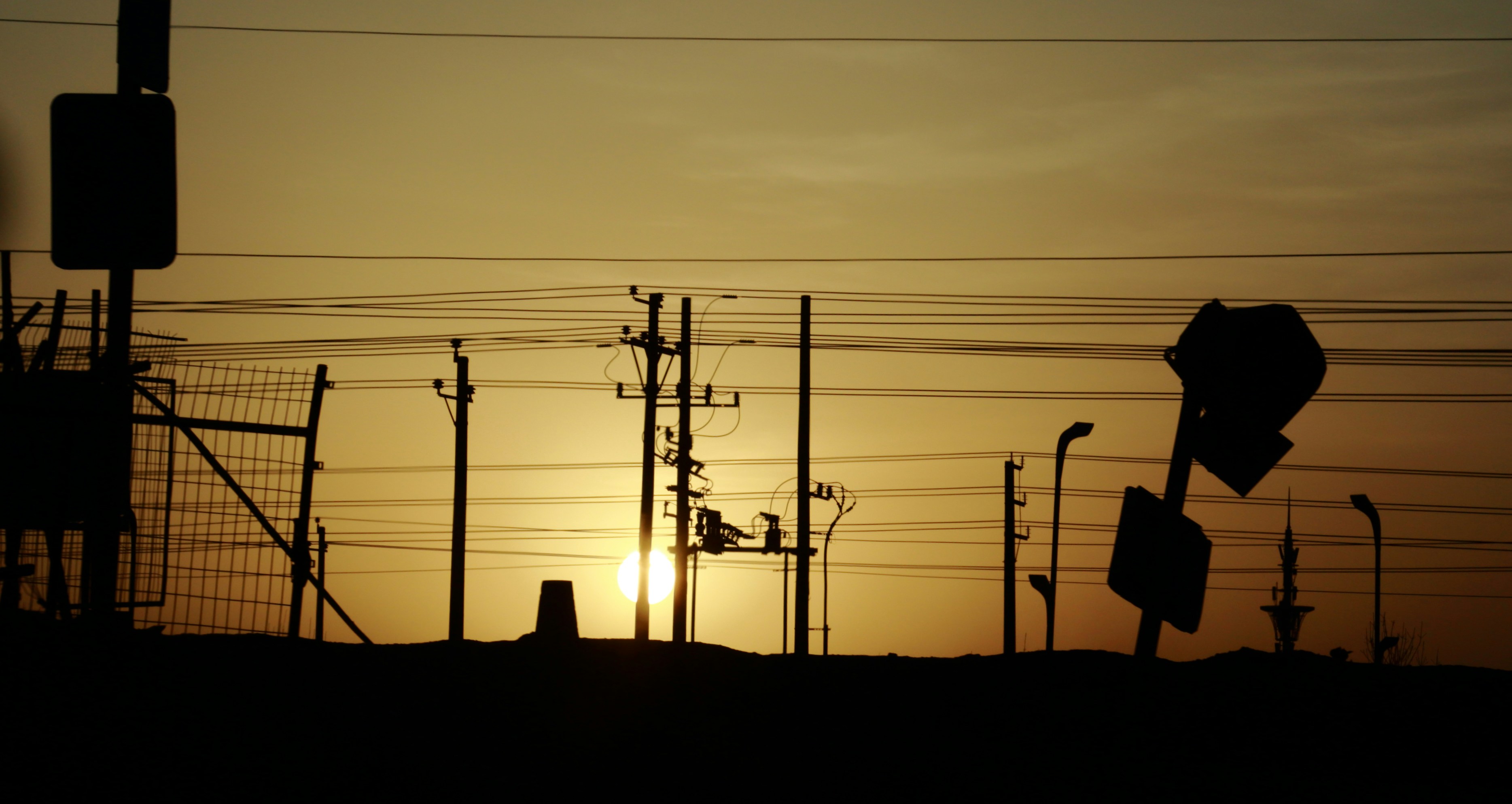The sun is setting in the distance behind a street sign