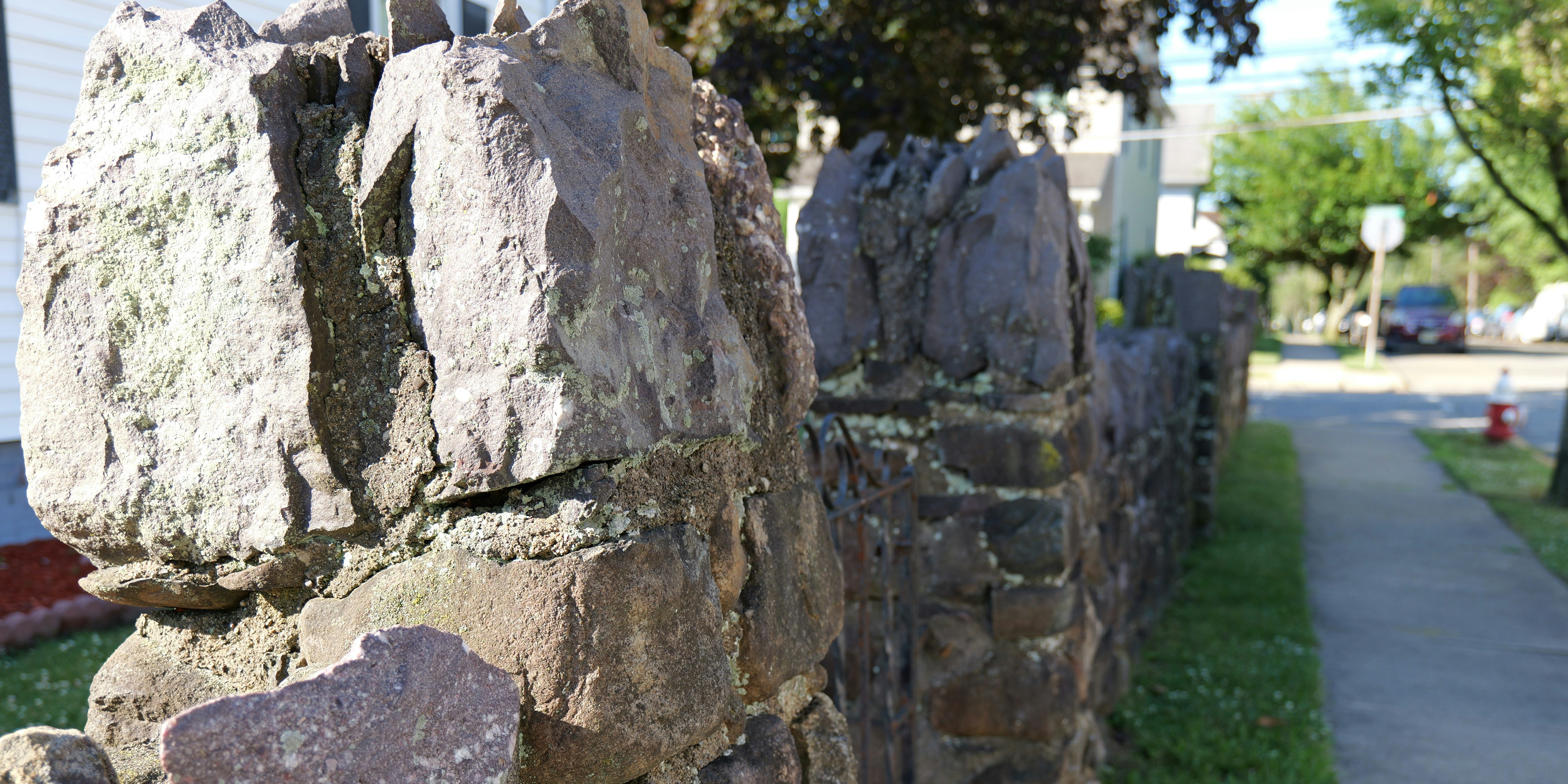 A rock wall next to a sidewalk and a house