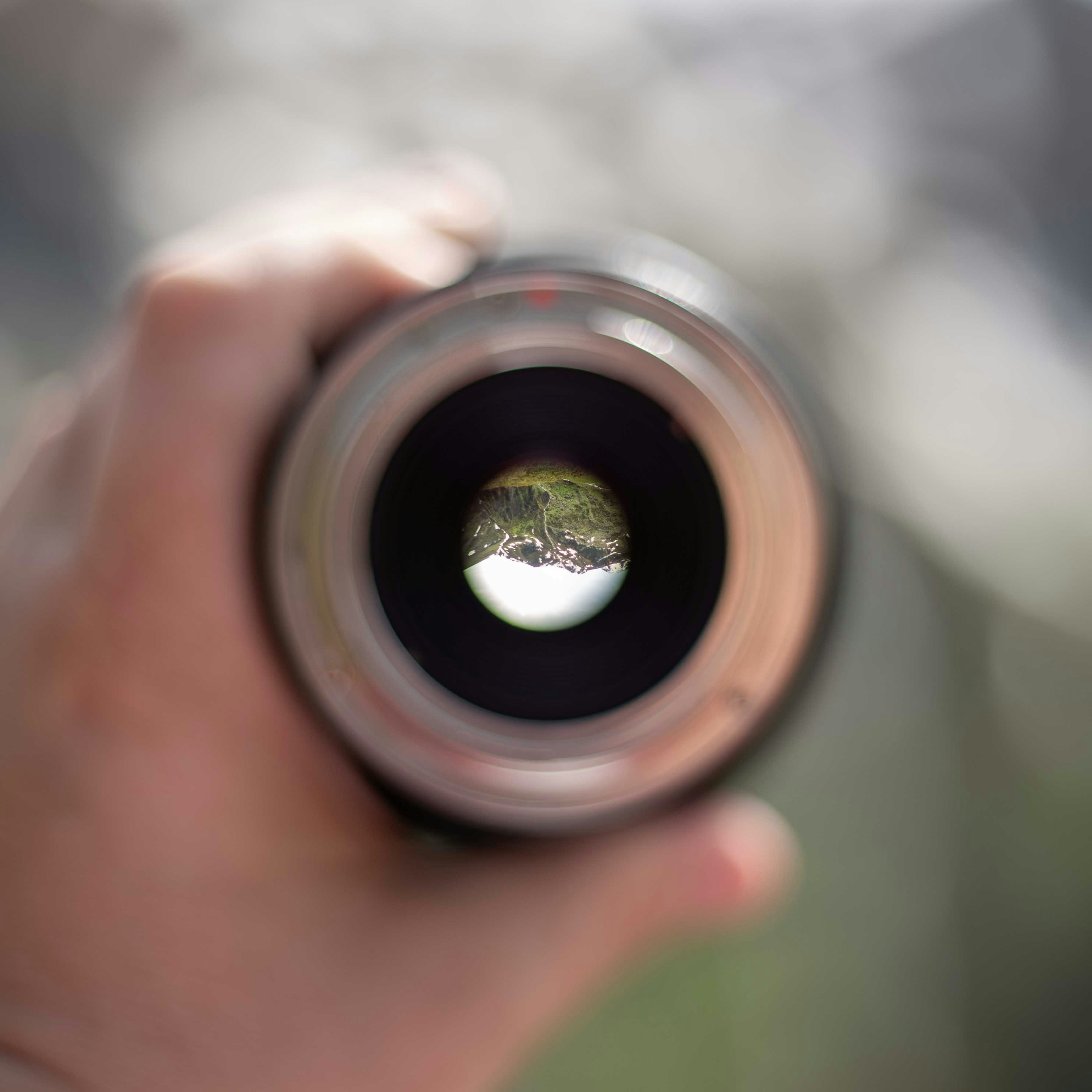 A person holding a camera lens with a tree in the background