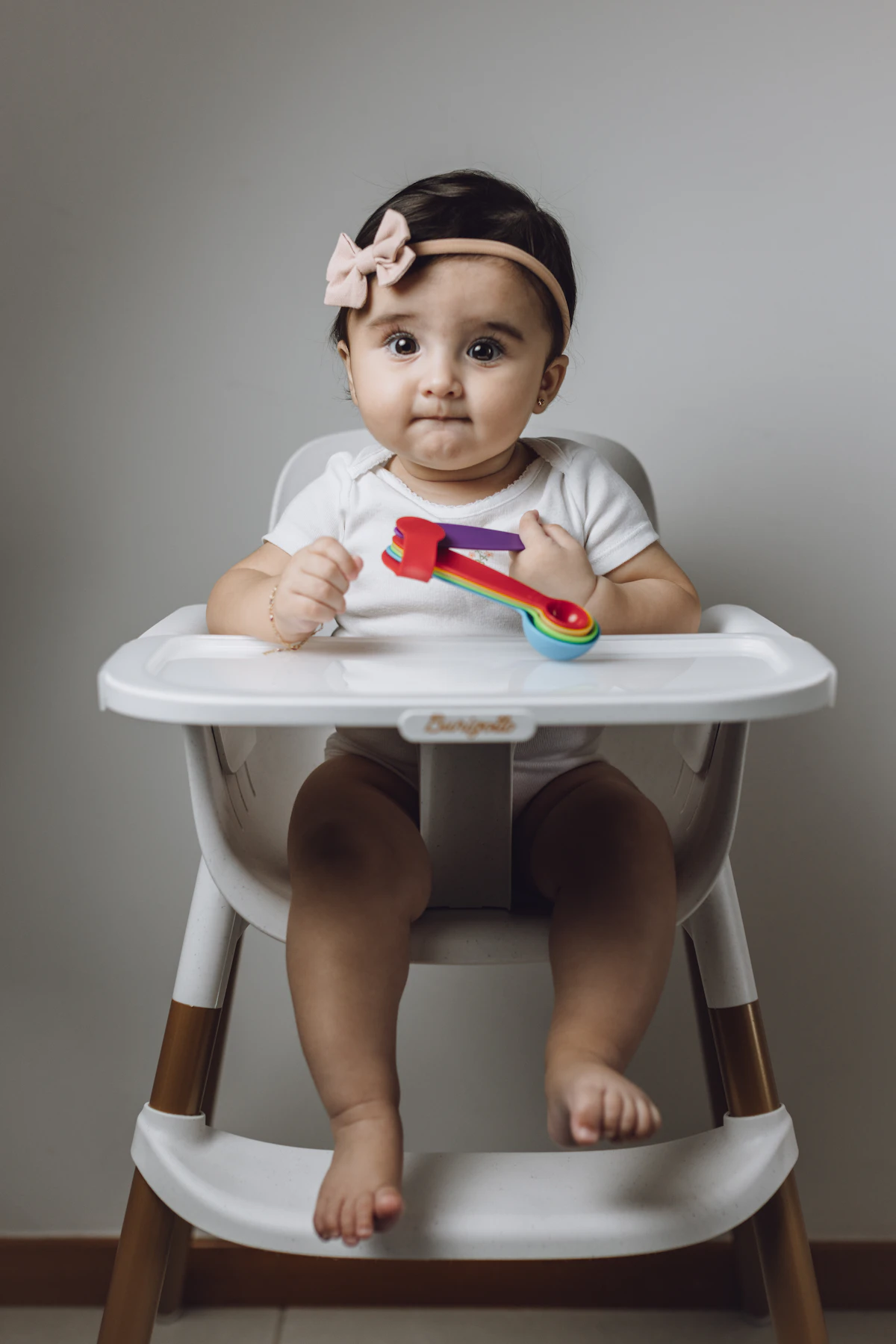 Baby sitting in a white plastic standard high chair with a fixed tray, a compact single-stage model