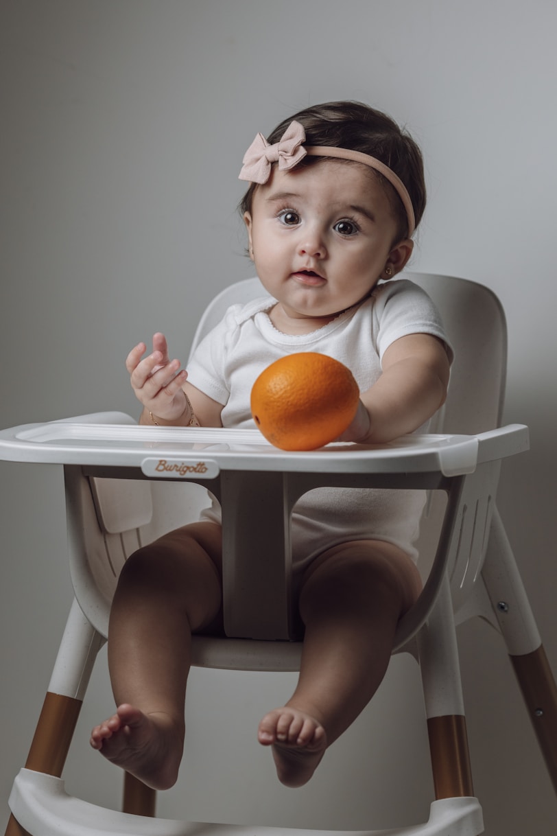 A baby sitting in a high chair with an orange