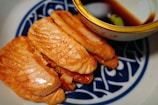 a blue and white plate topped with sliced fish next to a bowl of sauce