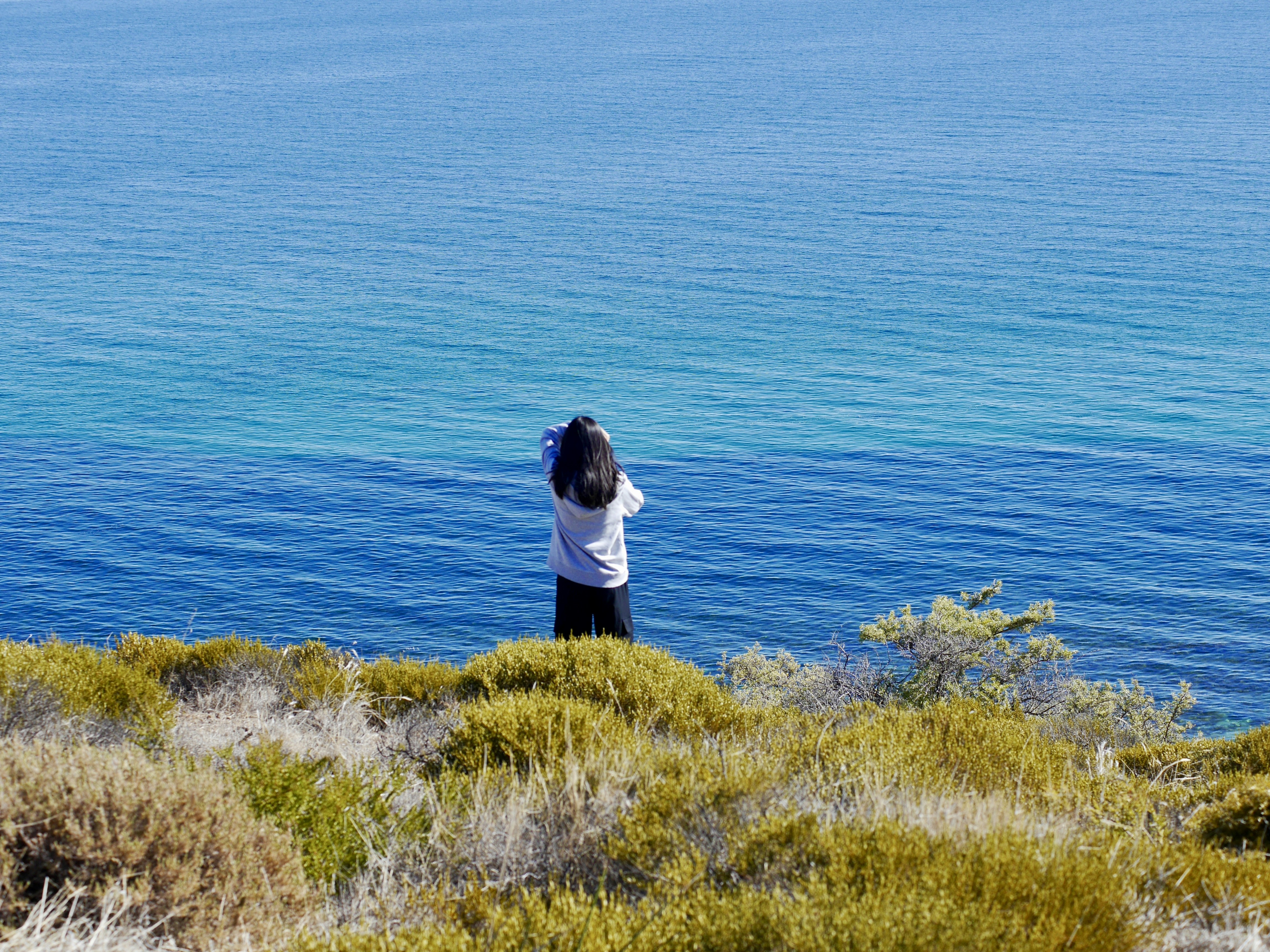a woman standing on top of a lush green hillside next to the ocean