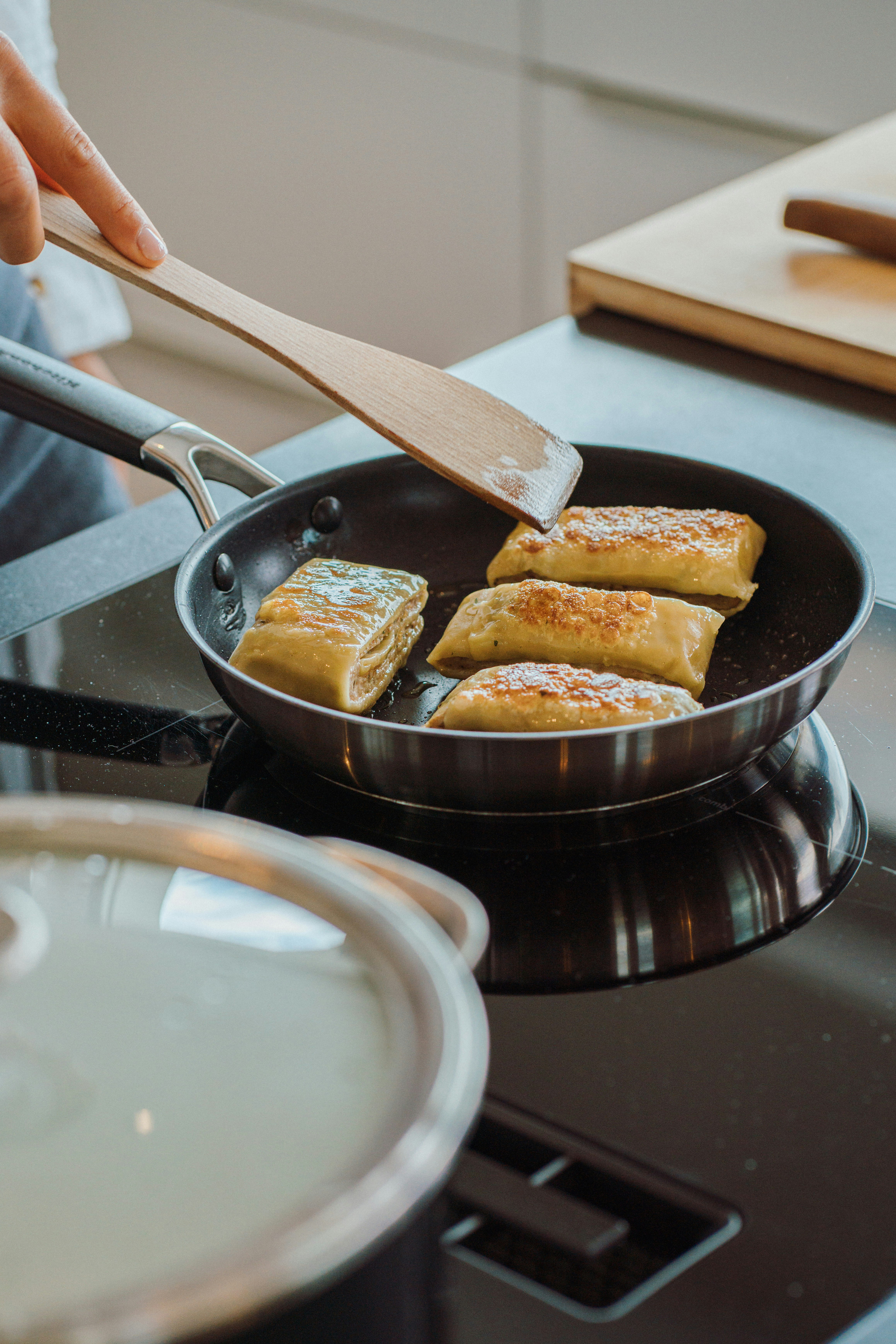 A person cooking food in a pan on a stove photo – Free Bread Image on ...