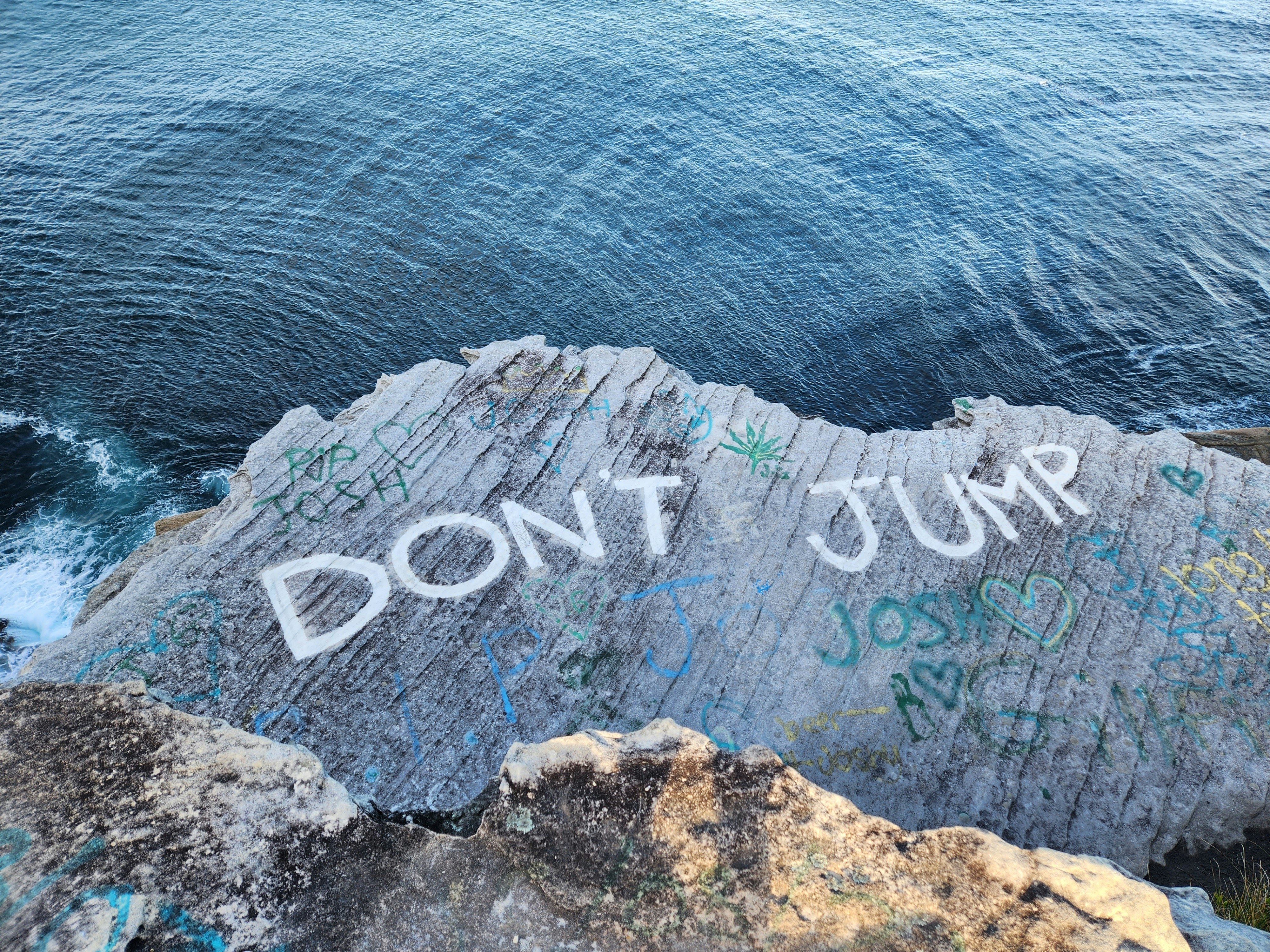 una roca con grafitis escritos junto al océano