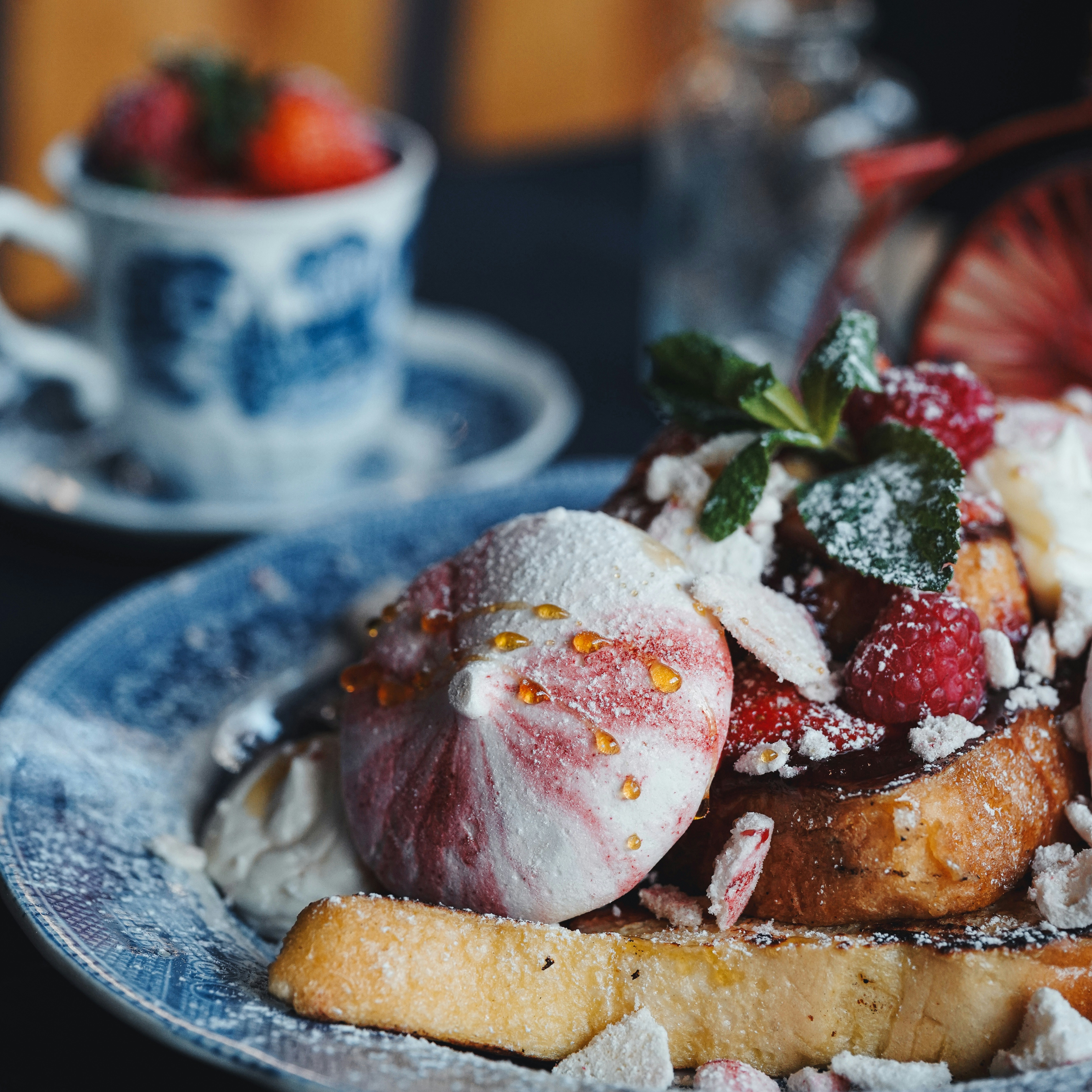Gourmet pancakes with berries, syrup drizzle and powdered sugar on dark plate