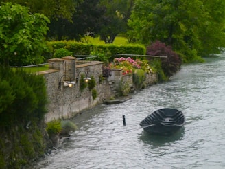 A black boat floating down a river next to a lush green forest