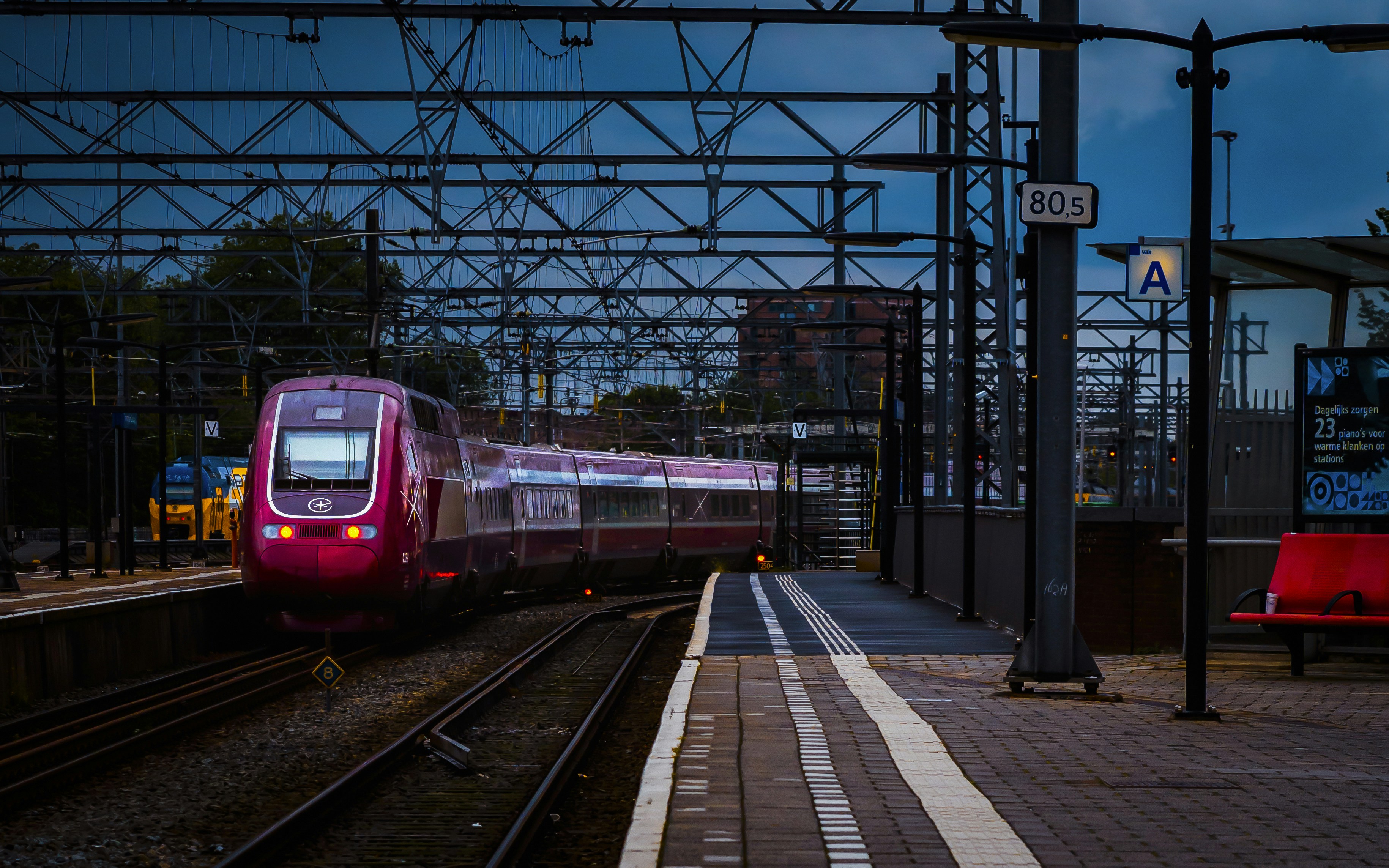 A red train traveling down train tracks next to a train station, 