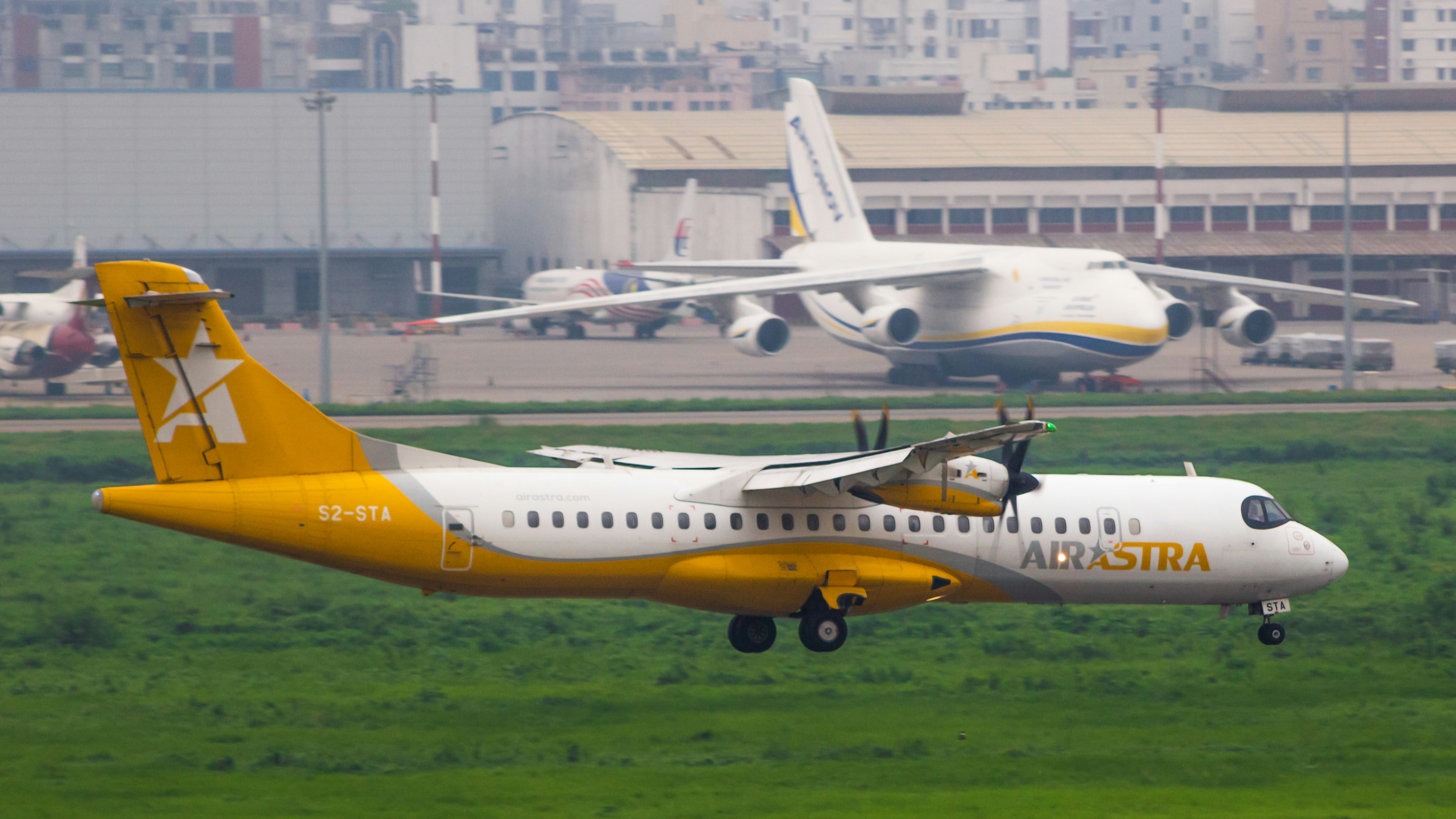 A plane taking off from an airport runway, Air Astra lands in VGHS while framing the An-124 behind!