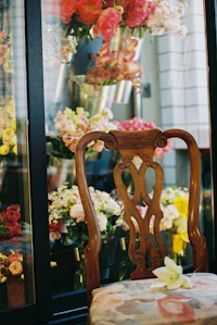 A wooden chair beside a studio window crowded with cut stems in the late afternoon